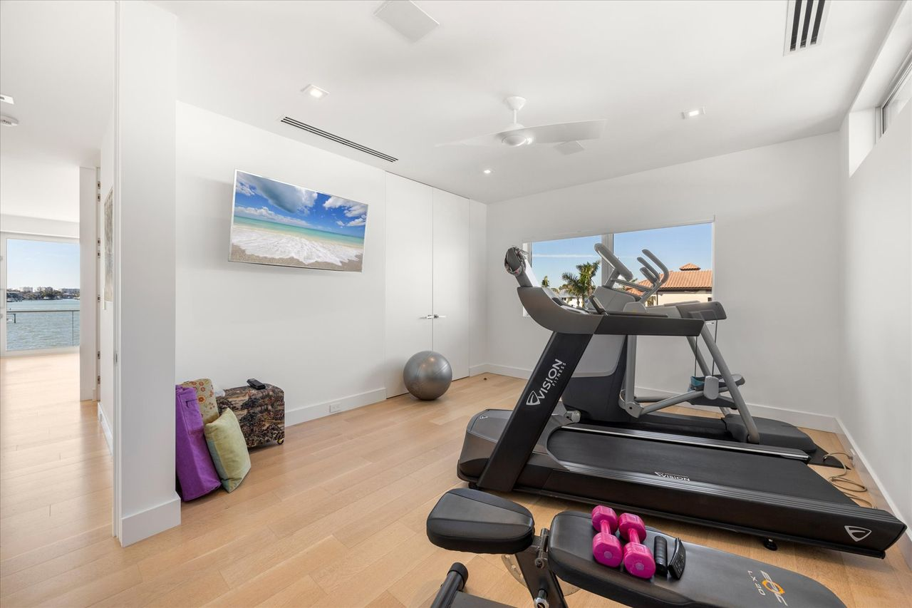 Another bedroom has been converted into a private fitness studio, completed with cardio equipment, free weights, and a wall-mounted TV.