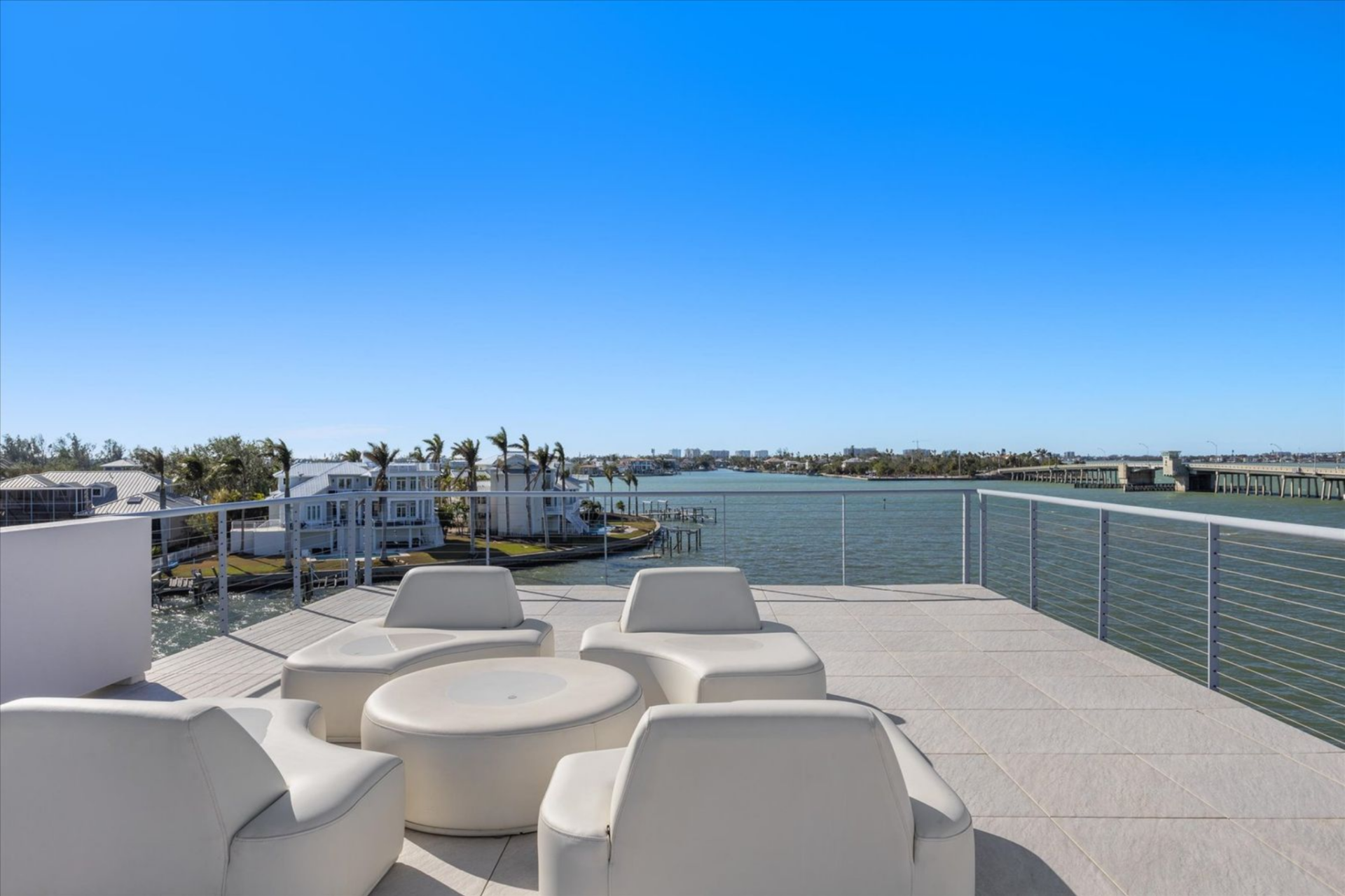 Low-profile seating is arranged to face the bay, while the wet bar anchors the deck as a functional hosting area, all framed by glass railings that keep the skyline and bridges fully in view.