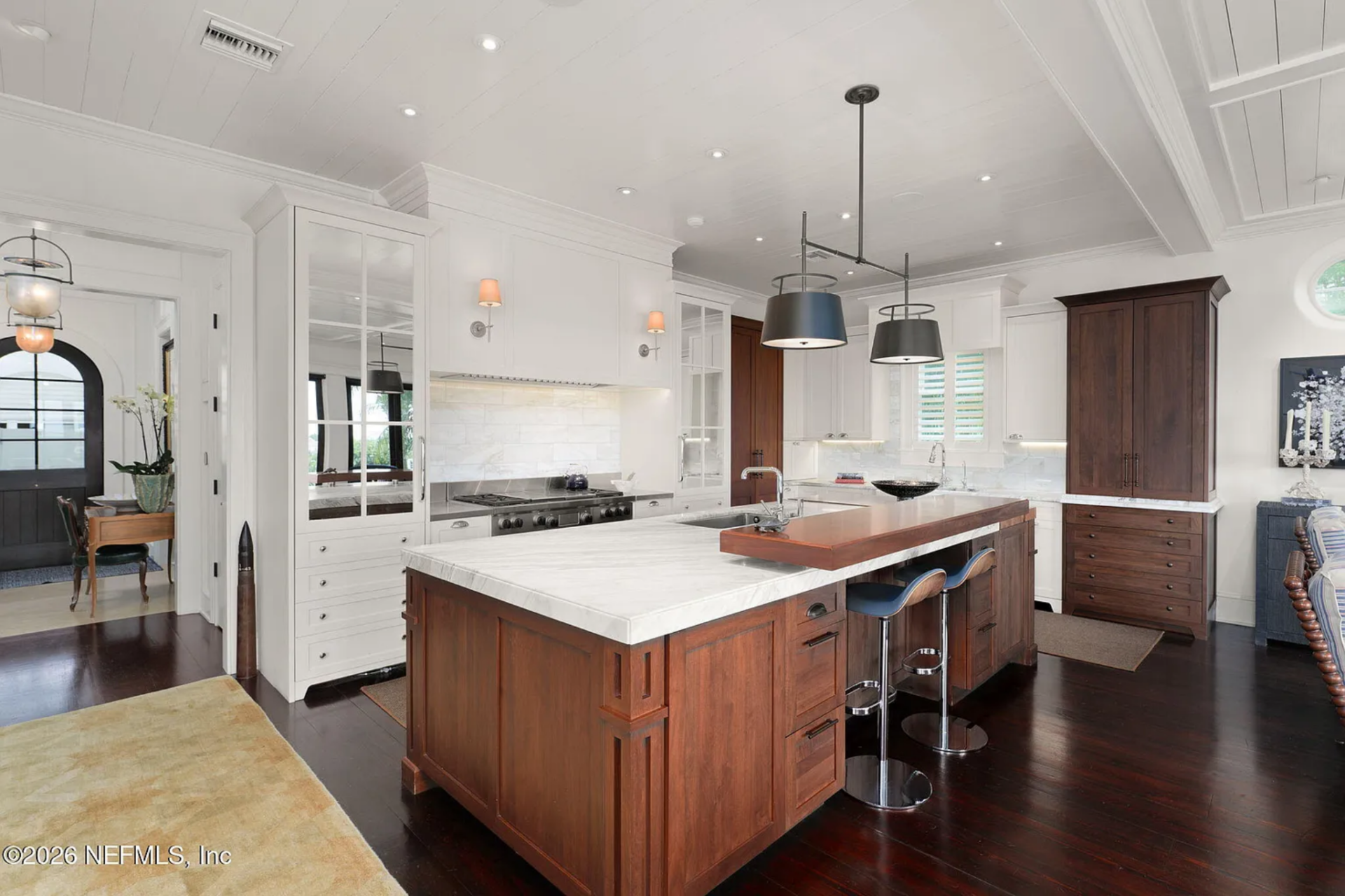 A large island is finished in rich wood cabinetry and topped with a thick slab of marble, with bar seating tucked beneath an extended wood counter.