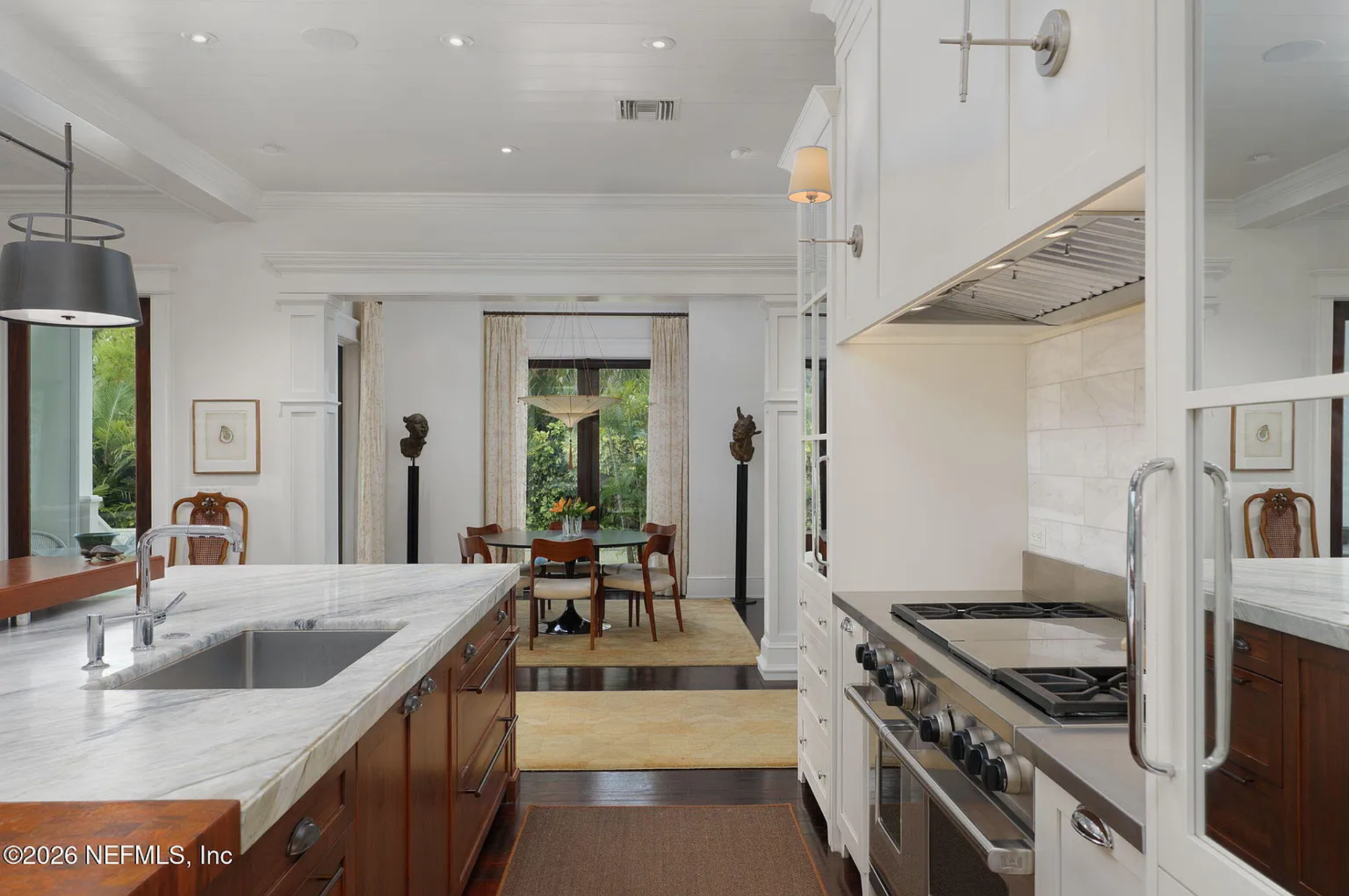 Along the perimeter, white cabinetry with glass-front uppers frames a professional-grade range and stone backsplash.