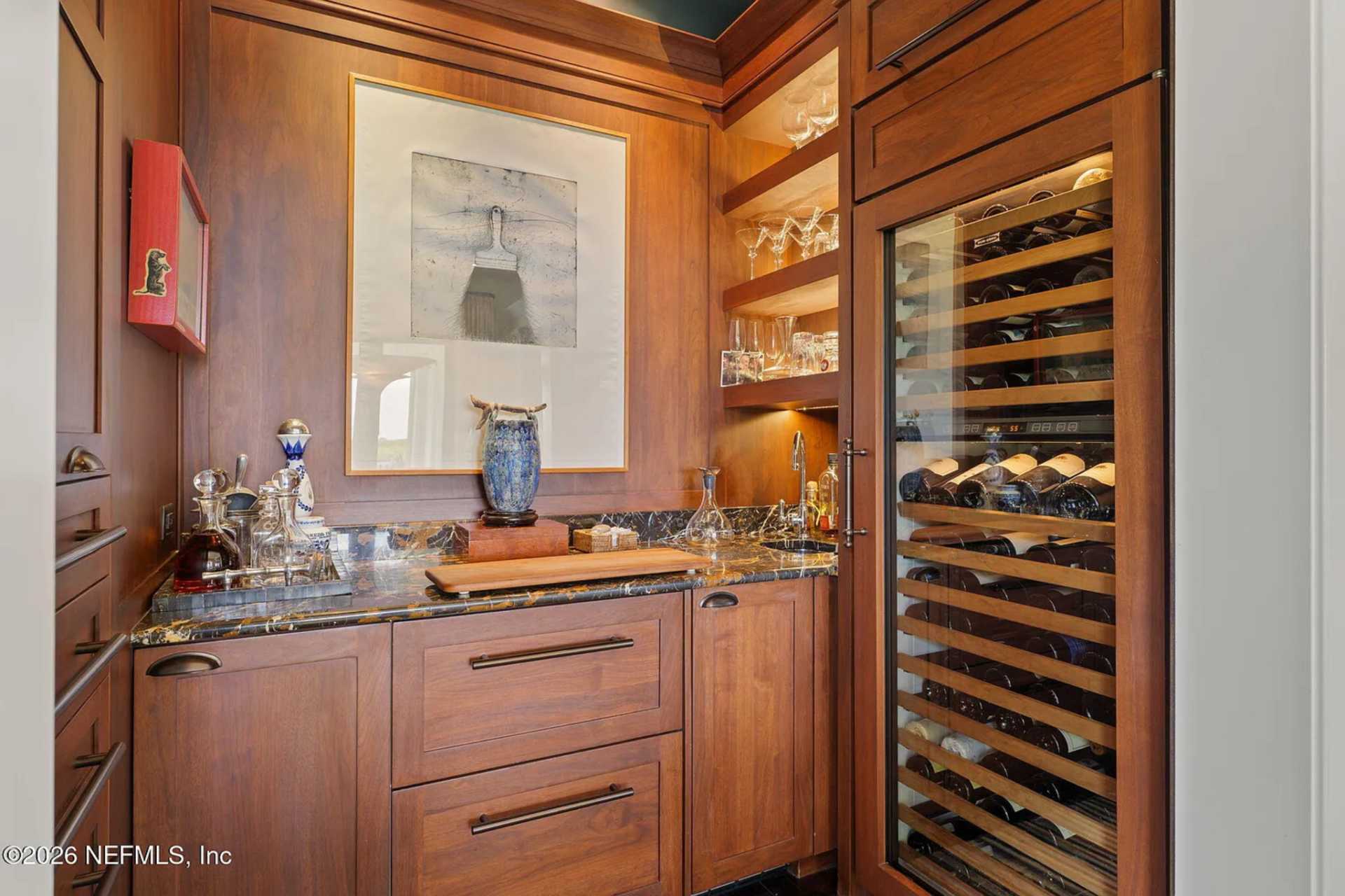 Open shelving displays glassware above a stone countertop, while a glass-front 140-bottle Sub-Zero wine cooler is integrated into the millwork.