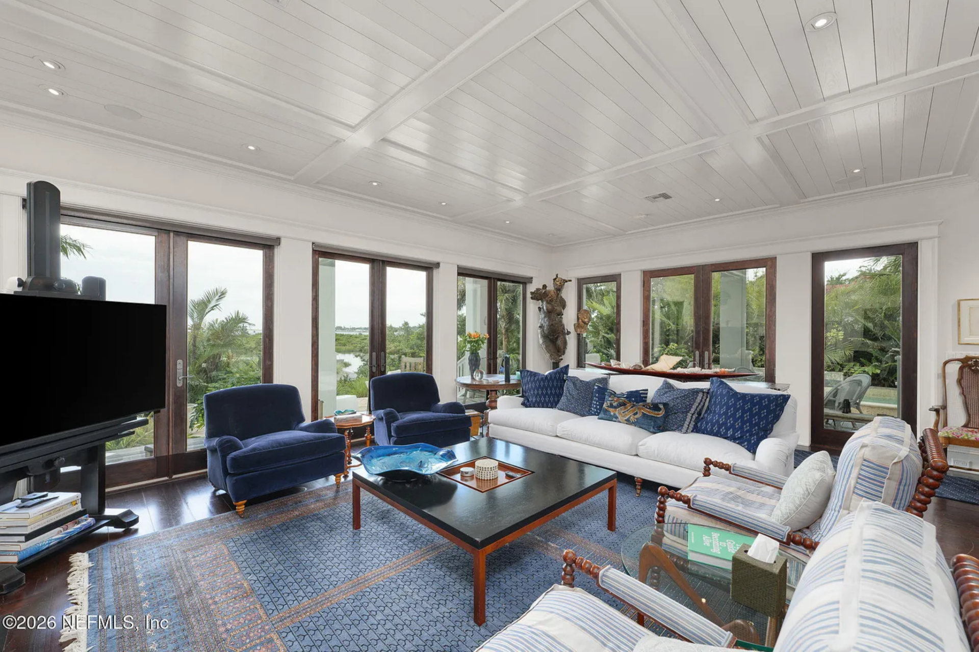 Seating is arranged around a large square coffee table, with upholstered armchairs, a tailored sofa, and deep blue lounge chairs creating a balanced conversation layout.
