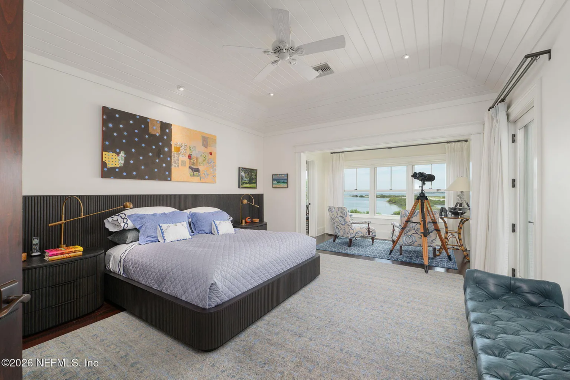 The bedroom itself centers on a low-profile bed framed by a dark paneled headboard wall, with matching nightstands and brass reading lamps positioned on either side.