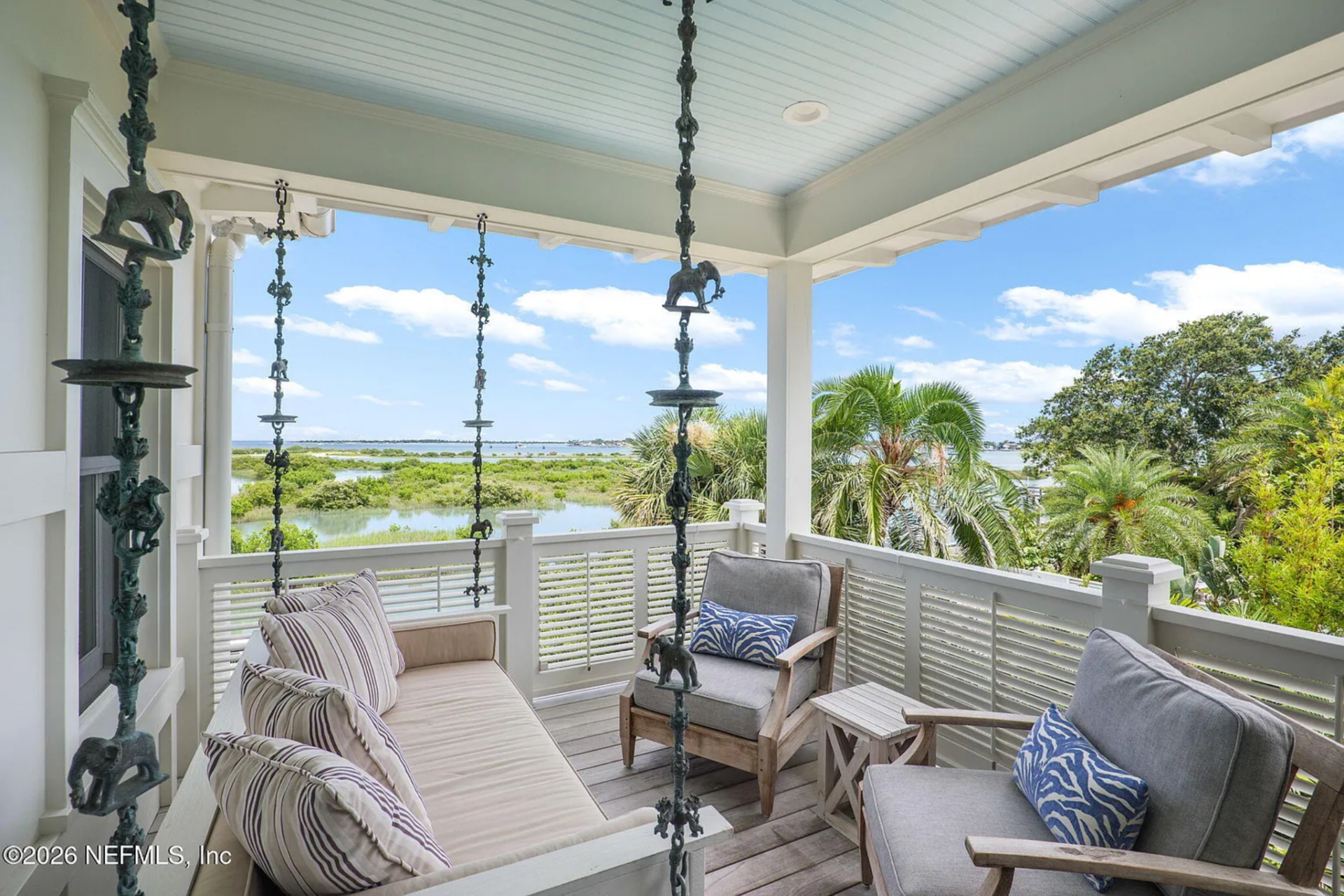 The porch ceiling and railings are finished in crisp white, with a hanging bench and armchairs gathered together.