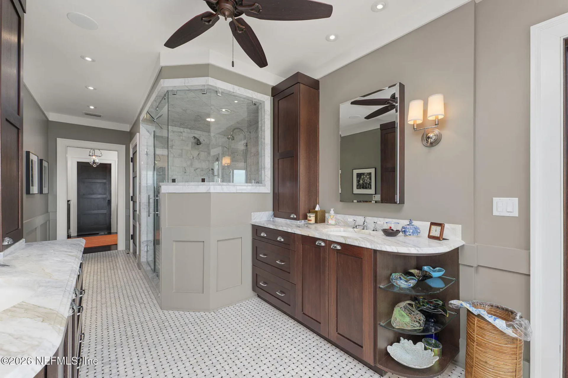 A glass-enclosed shower with marble tile sits further down the space, maintaining clear sightlines and consistent finishes throughout.