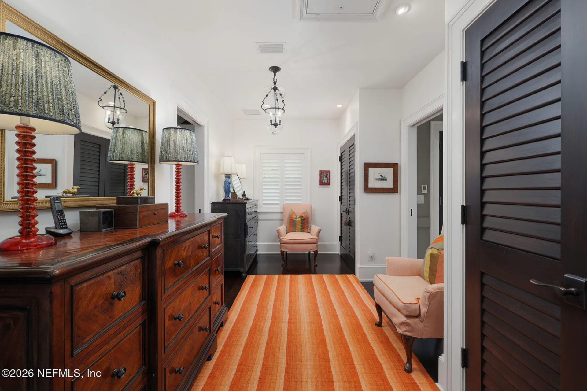 The walk-in closet functions as its own dressing room, fitted with dark wood dressers, louvered doors, and built-in storage lining both sides.