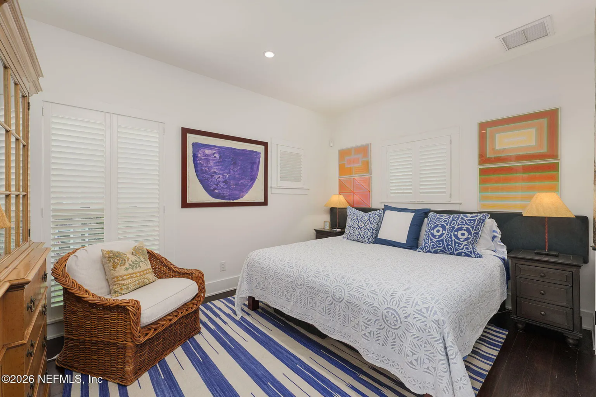 Bedroom with a crisp coastal palette, with a king bed dressed in white bedding, blue accent pillows, and a striped blue-and-cream area rug underfoot.