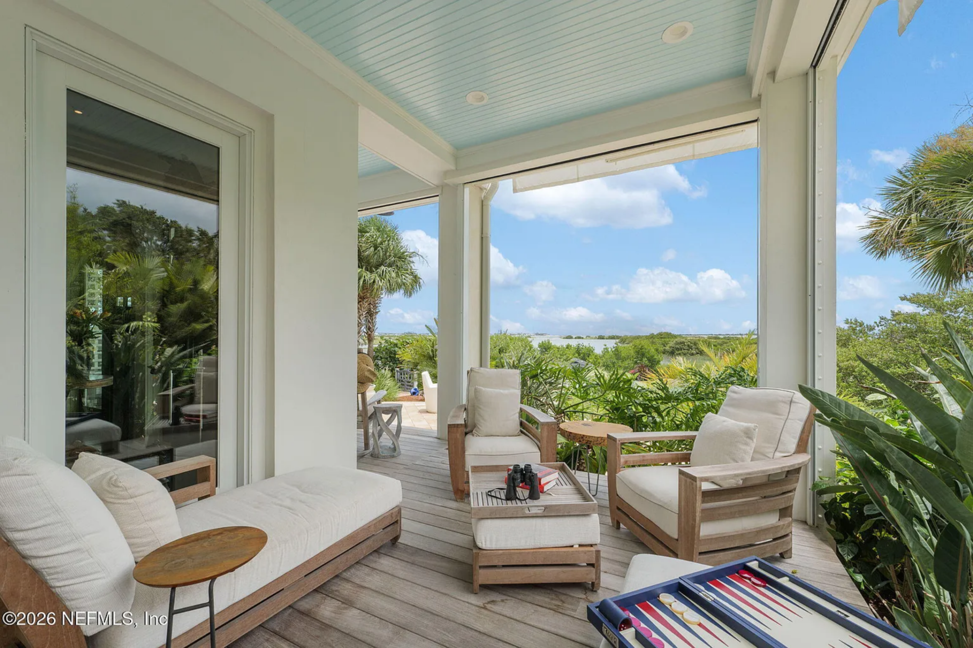 A covered deck with a soft blue beadboard ceiling offers a shaded place to relax with cushioned lounge seating and side tables.