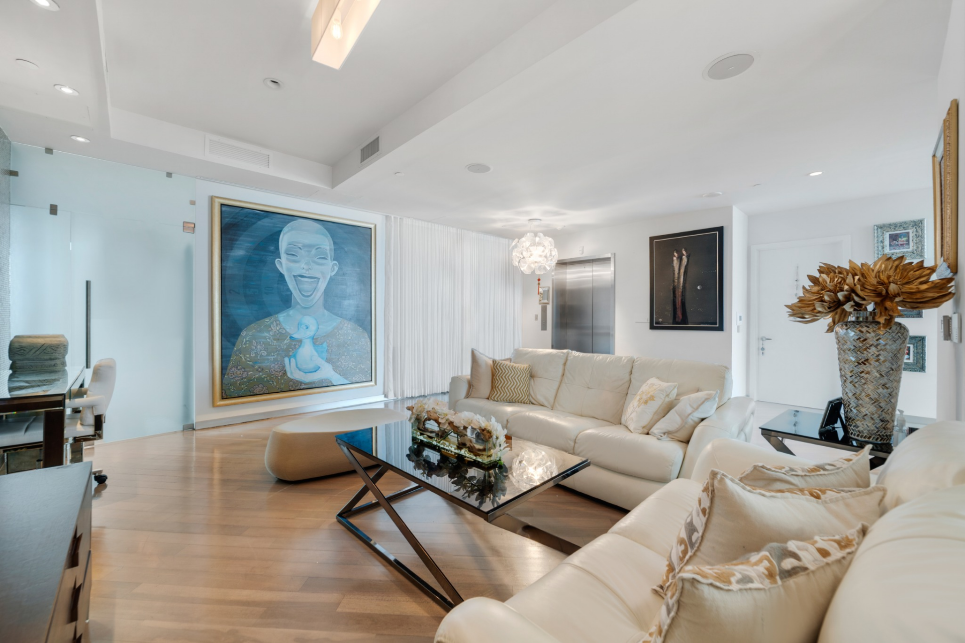From there, the space opens into the formal living room, where neutral leather sofas surround a glass-top coffee table with angular metal legs. 