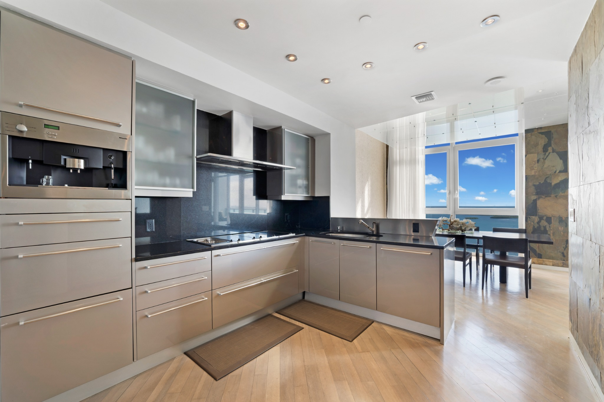 Flat-panel cabinetry in a soft metallic finish lines the walls, paired with black stone countertops and a matching backsplash that runs behind the cooktop. 