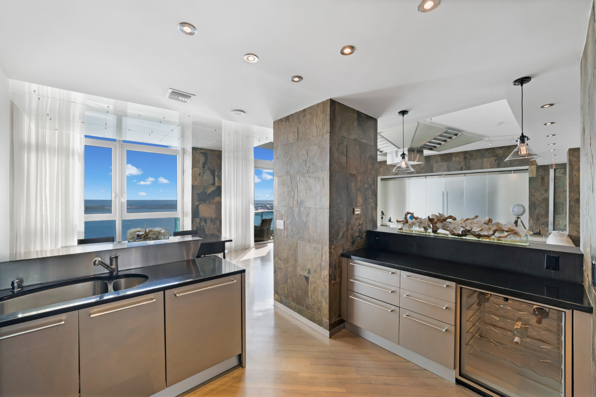 The layout wraps into a secondary counter with an undercounter wine refrigerator and additional storage, creating a natural prep and service area just steps from the built-in bar.