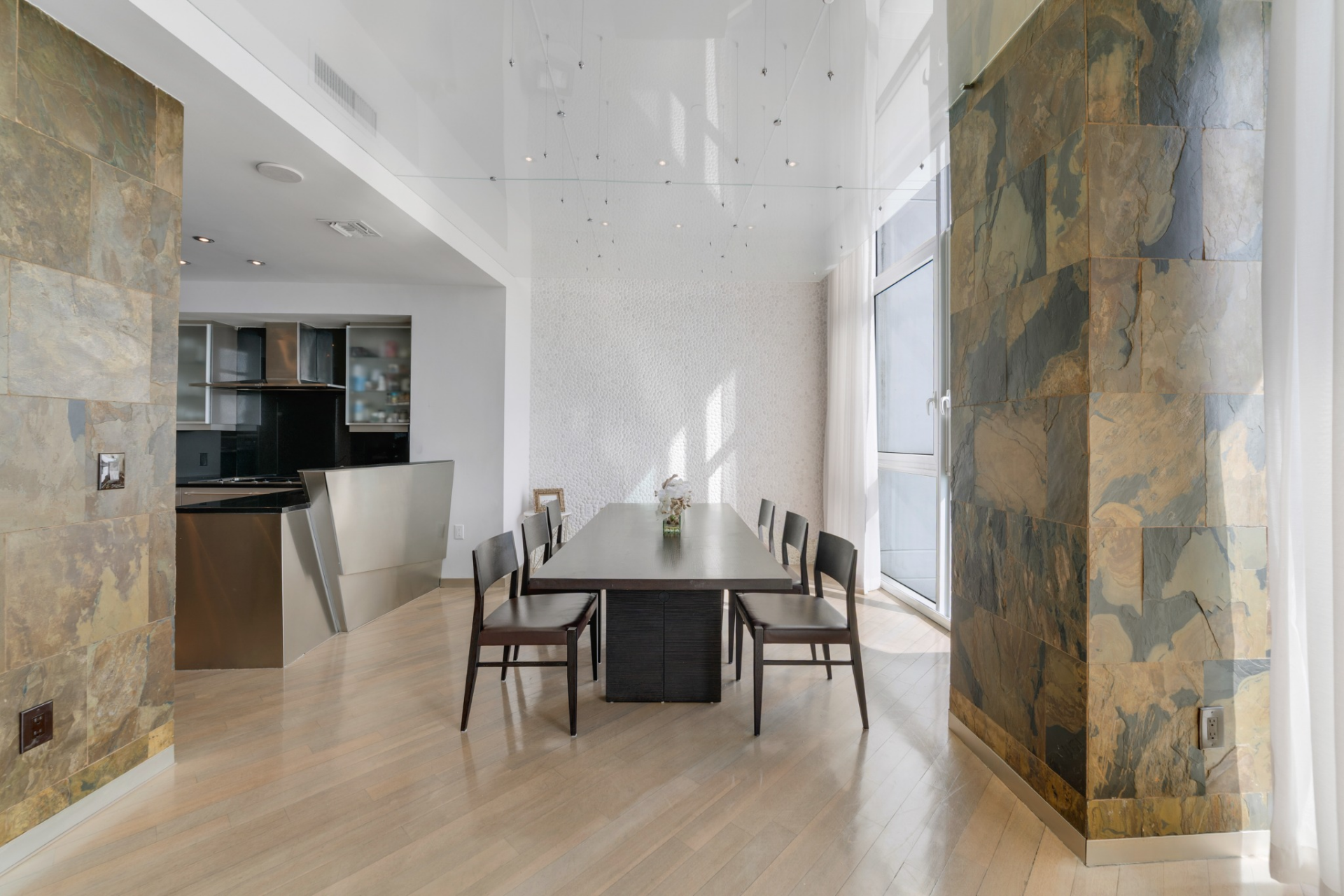 Along the windows, the dining area is positioned between the kitchen and the glass-lined exterior walls. A long, dark wood table sits surrounded by six streamlined chairs that keep the space clean and linear.
