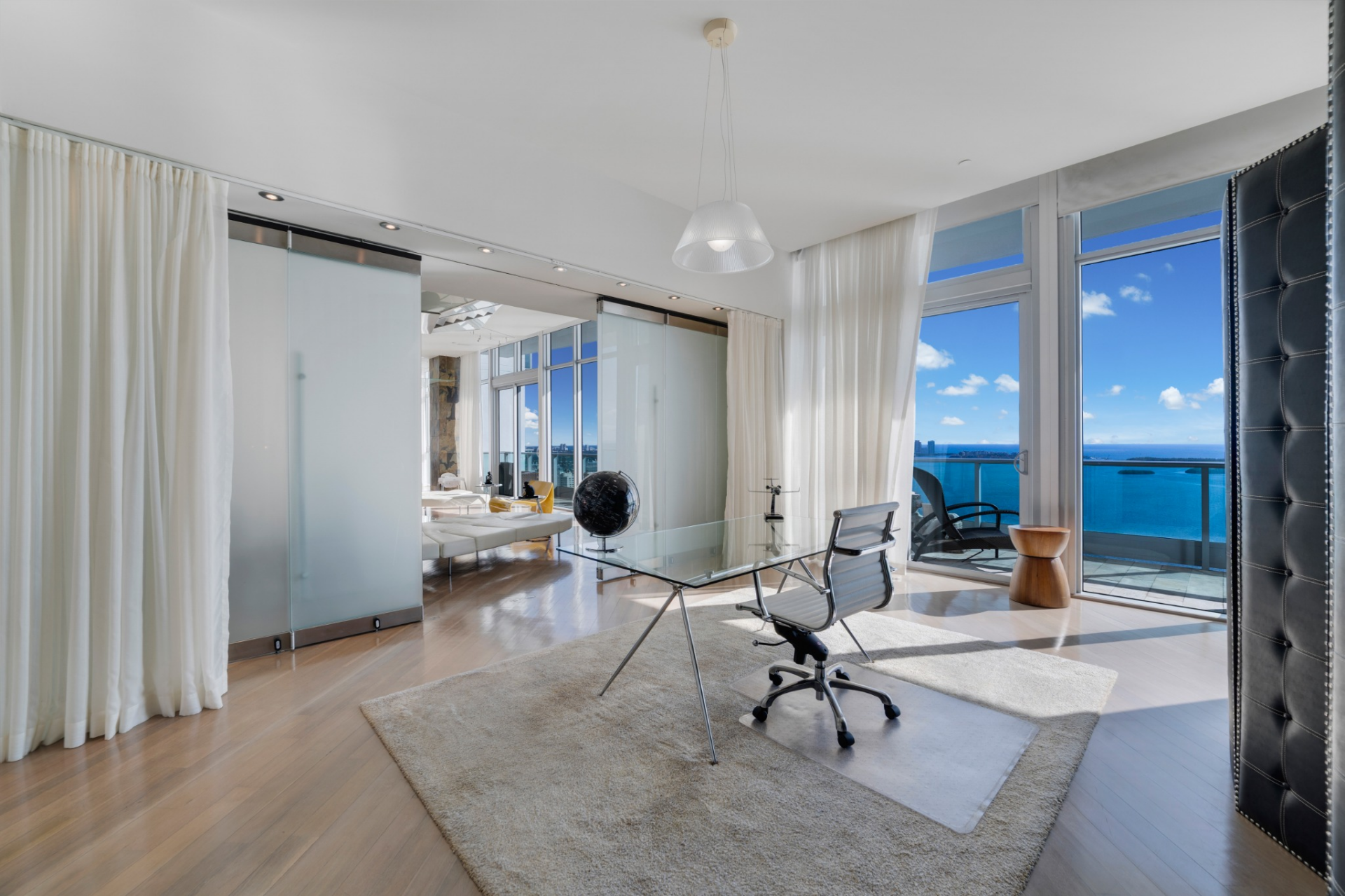 The suite opens into a dedicated sitting and workspace framed by floor-to-ceiling glass overlooking the bay. 