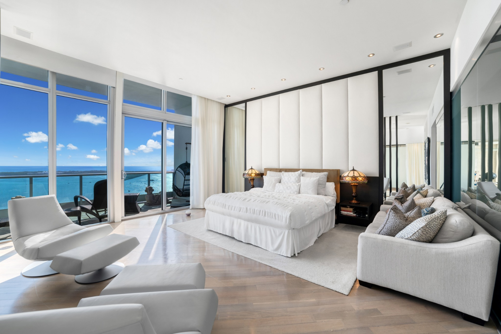 A white upholstered bed with layered bedding sits on a soft area rug in the middle, framed by matching nightstands and warm-toned lamps. 