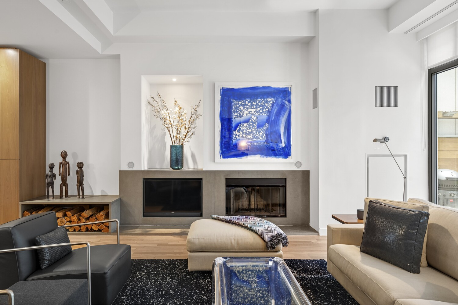 Across from the couch, a wood-burning fireplace is built into a clean-lined wall, with a low hearth and integrated niches.