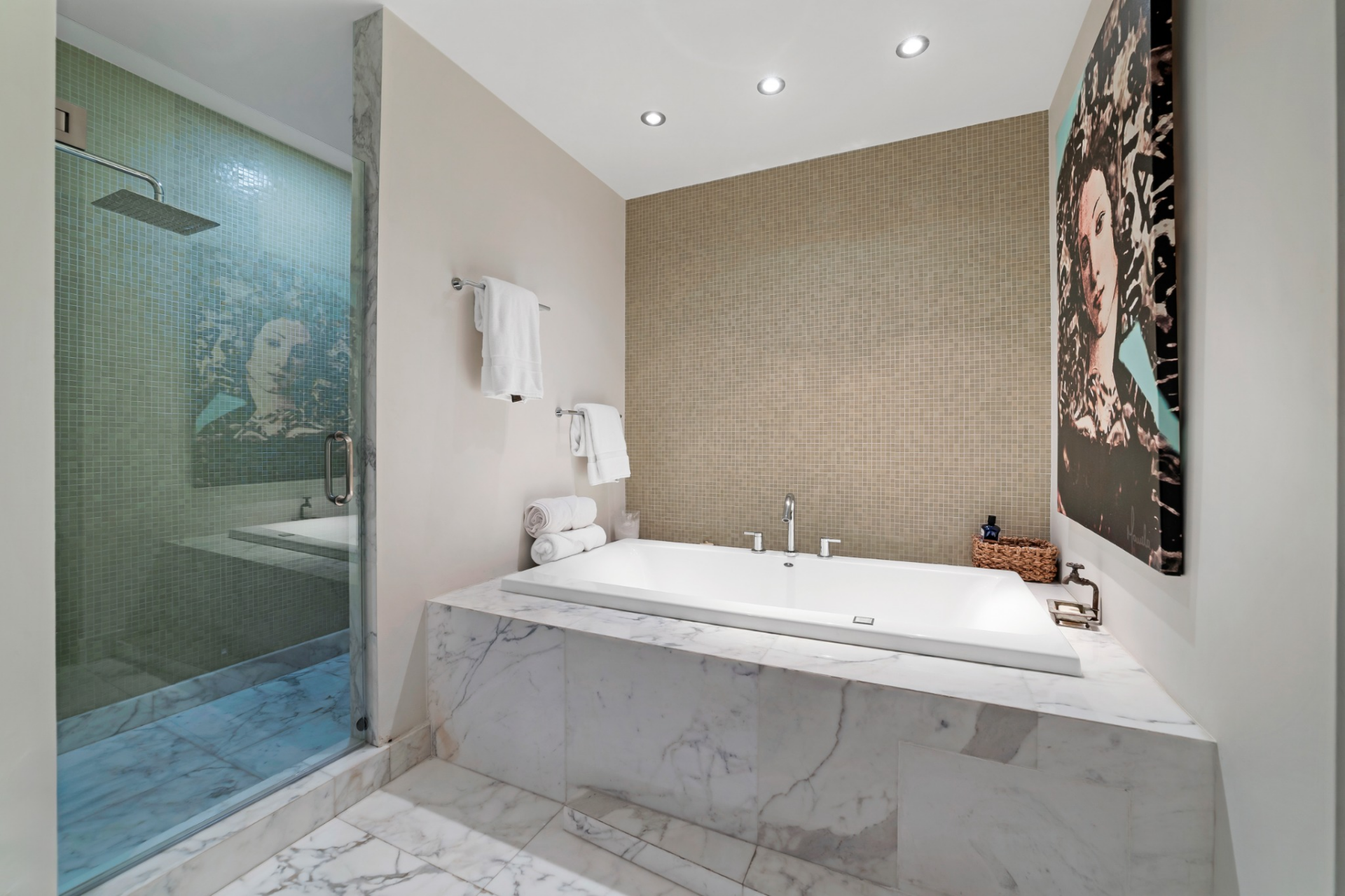 Bathroom with a built-in soaking tub wrapped in veined stone that extends across the floor next to a glass-enclosed shower.