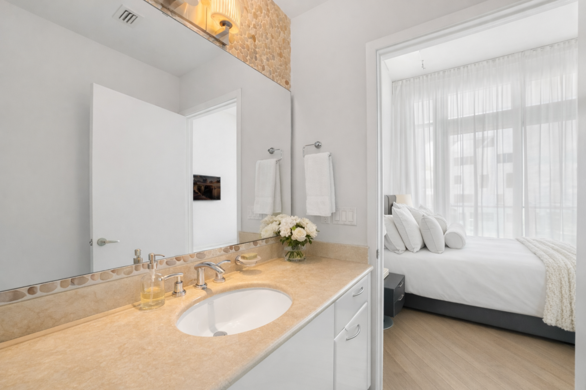 The bathroom continues the understated design with a single-sink vanity topped in warm-toned stone and framed by a full-width mirror. 