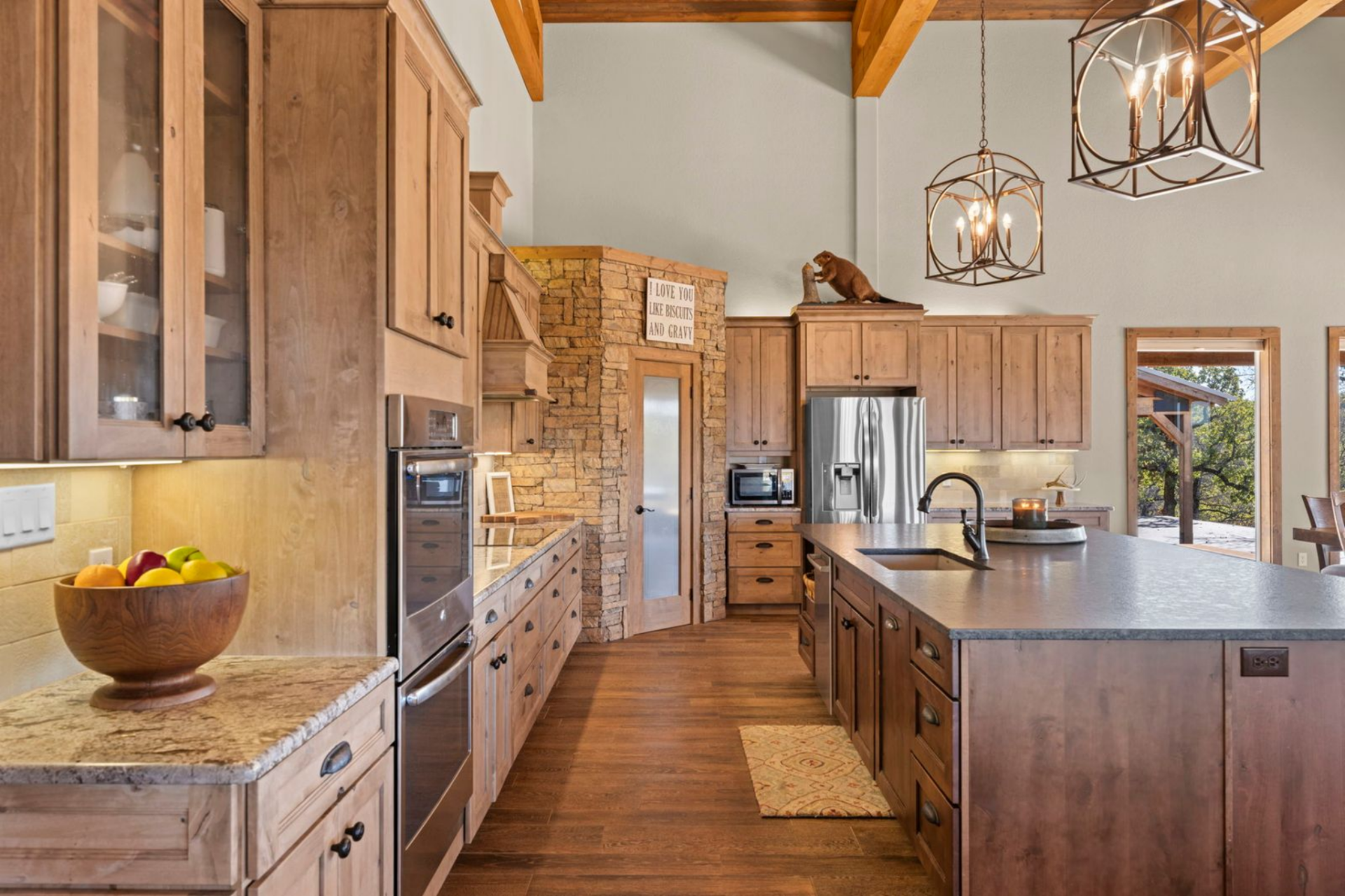 The kitchen sits in the left corner of the great room with a large central island topped with a dark stone counter and lined with barstools, a built-in sink, and plenty of room for guests to linger while meals come together.