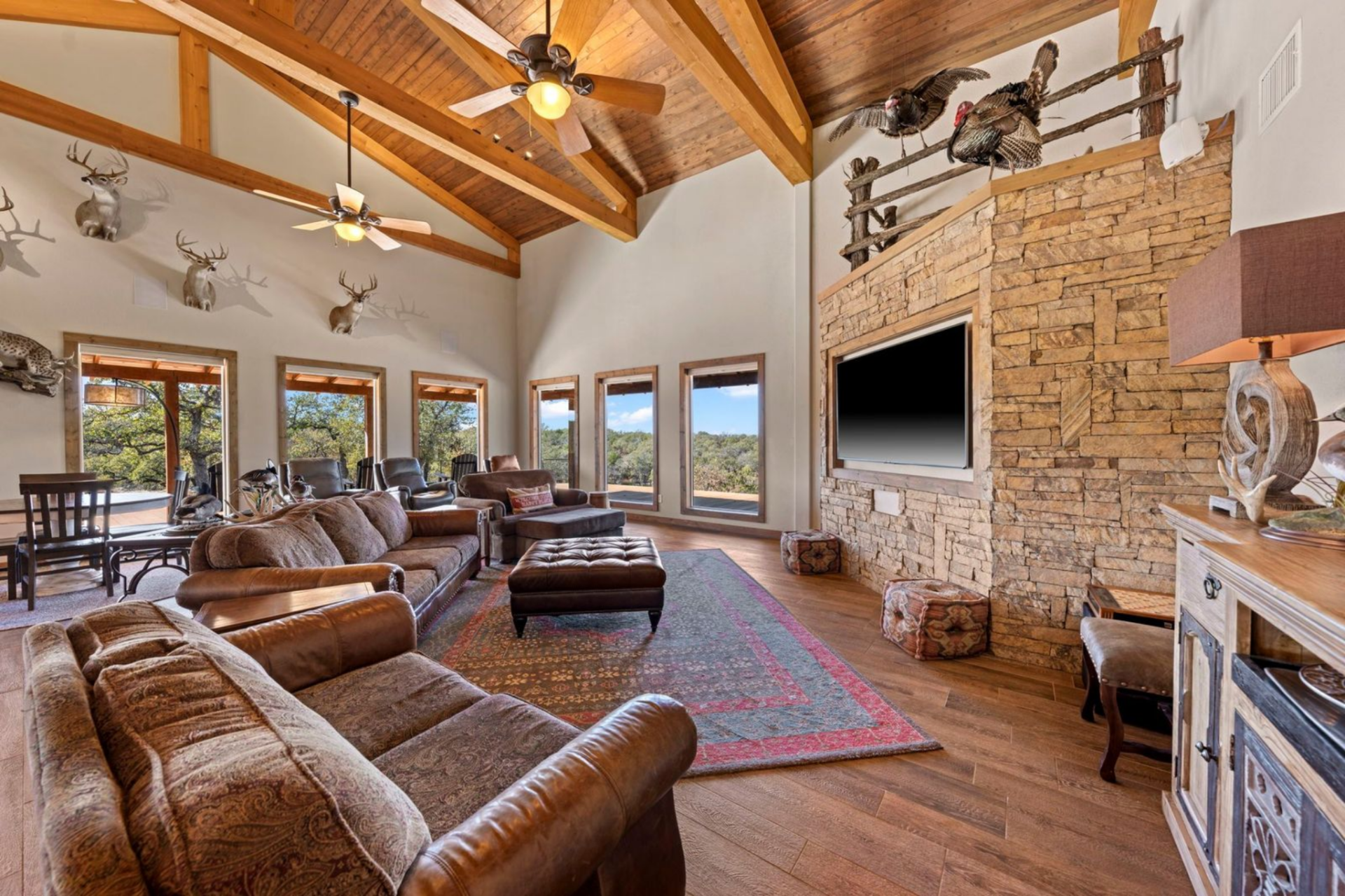 The living space centers around a floor-to-ceiling stone wall with a mounted television set into the masonry and a collection of oversized leather sofas and armchairs wraps around a large ottoman