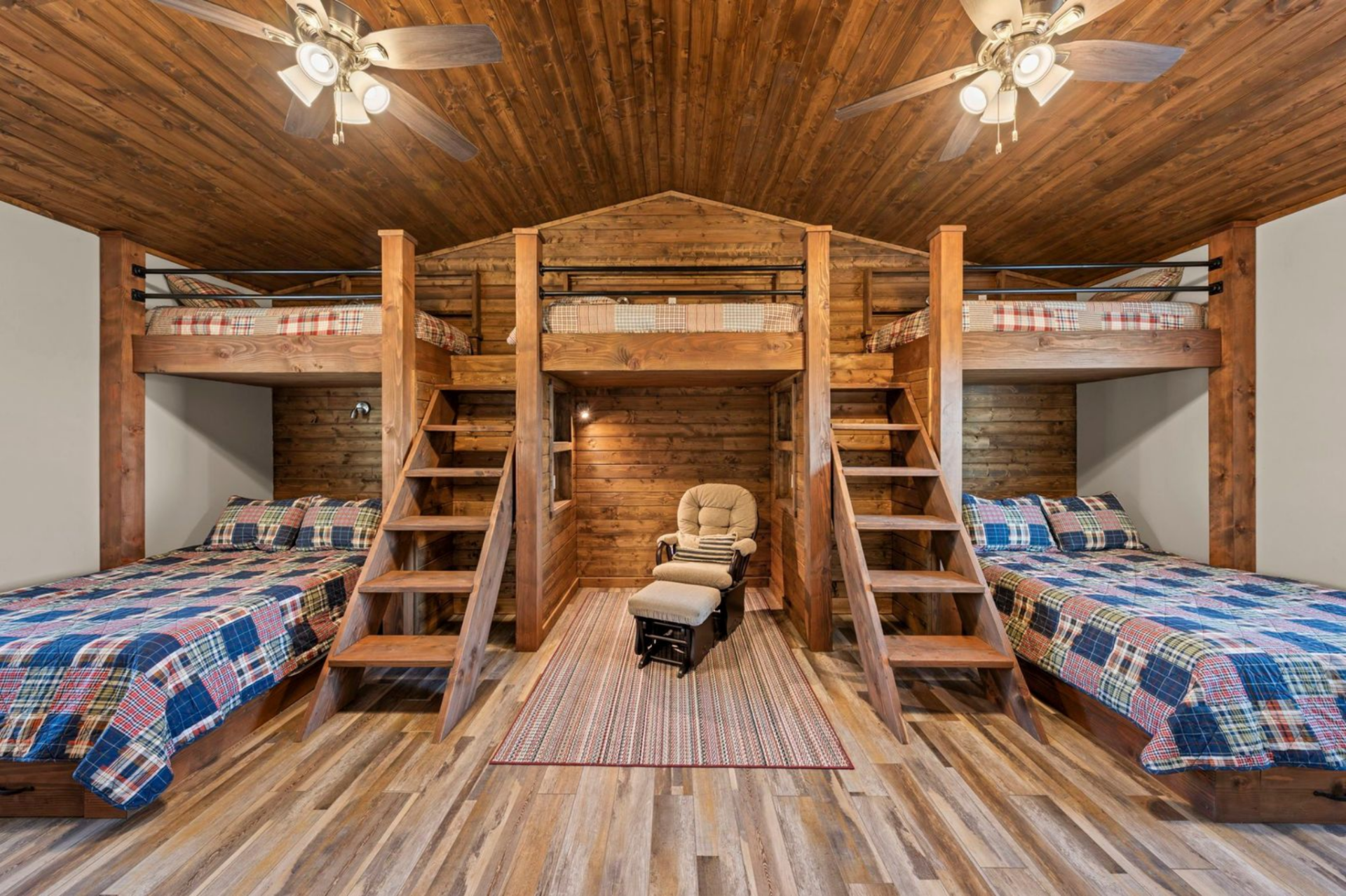 The space features two identical sides of custom bunkbeds, with two full beds below and twin bunks above, each accessed by built-in wooden ladders and framed by solid timber posts.