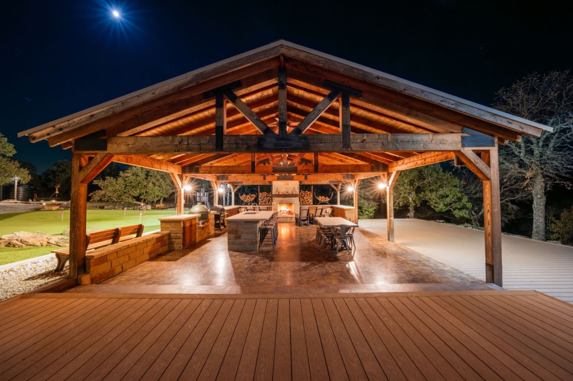 Next to the green is an open-air pavilion featuring a full outdoor kitchen, a long dining table, and a fireplace.