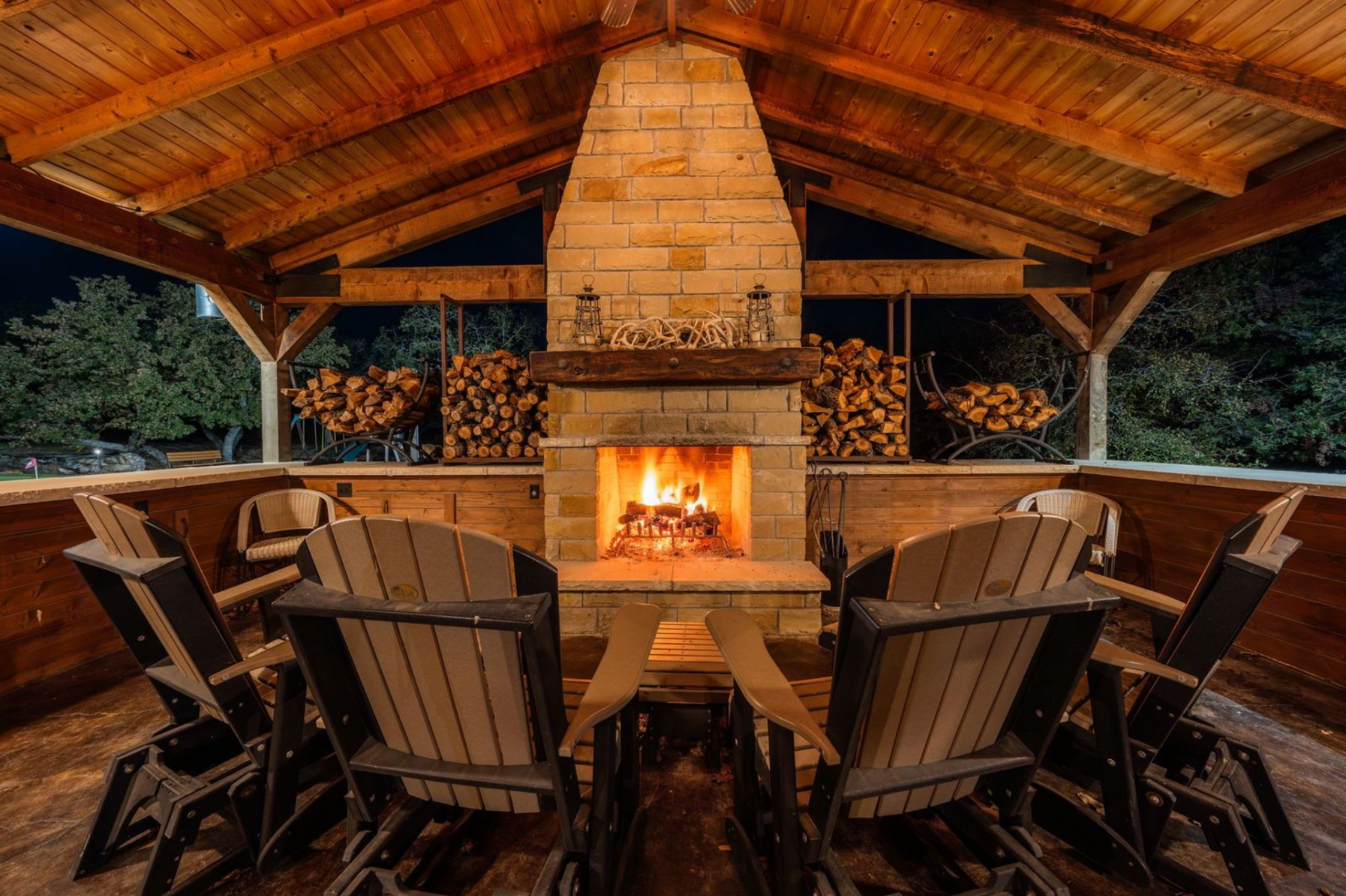 At the back of the pavilion, the wood-burning fireplace creates a warm focal point, framed by stacks of firewood ready for use.