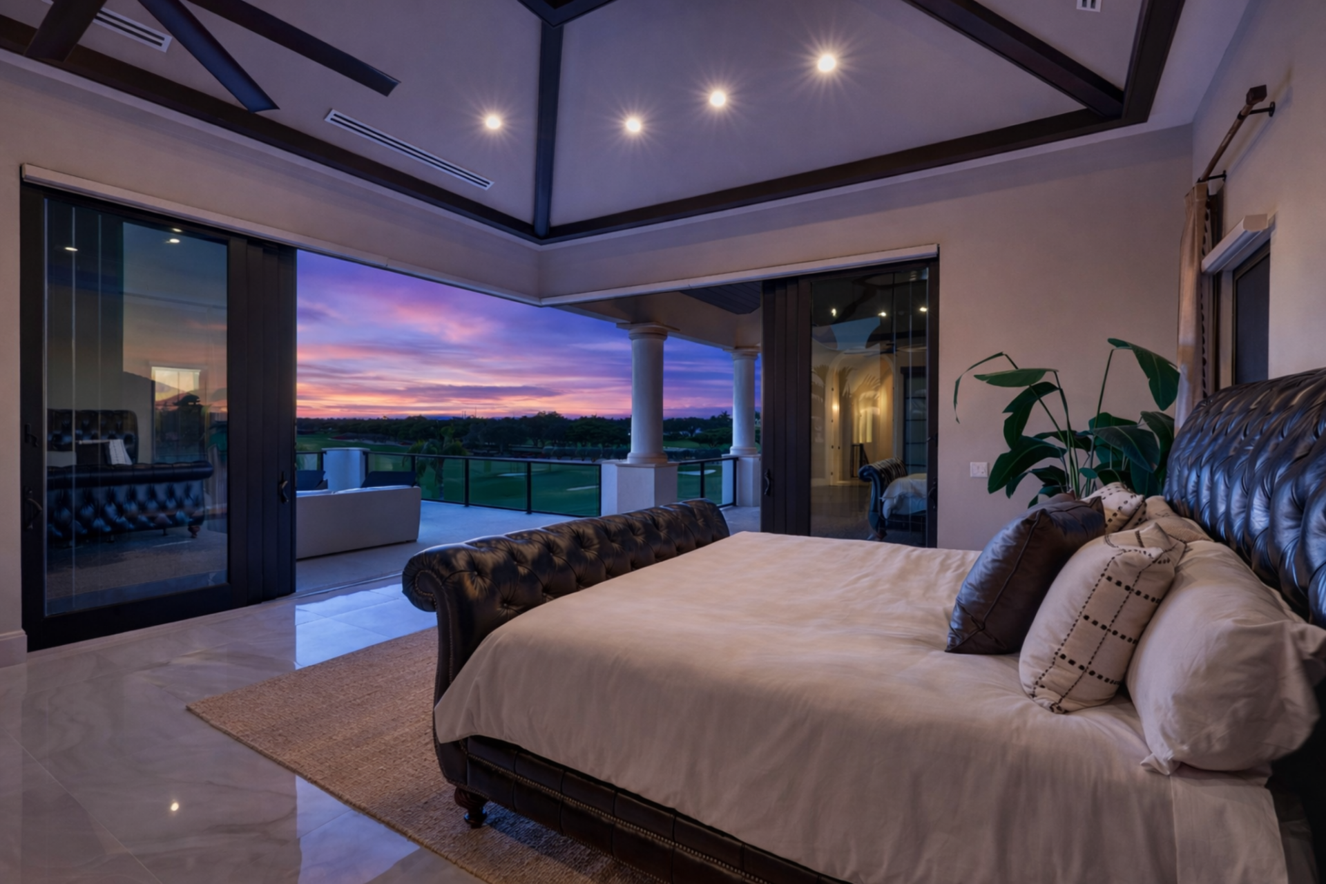 In the bedroom, oversized sliding glass doors retract completely, opening to views of the golf course and recessed lighting adds architectural depth above the leather-upholstered bed.