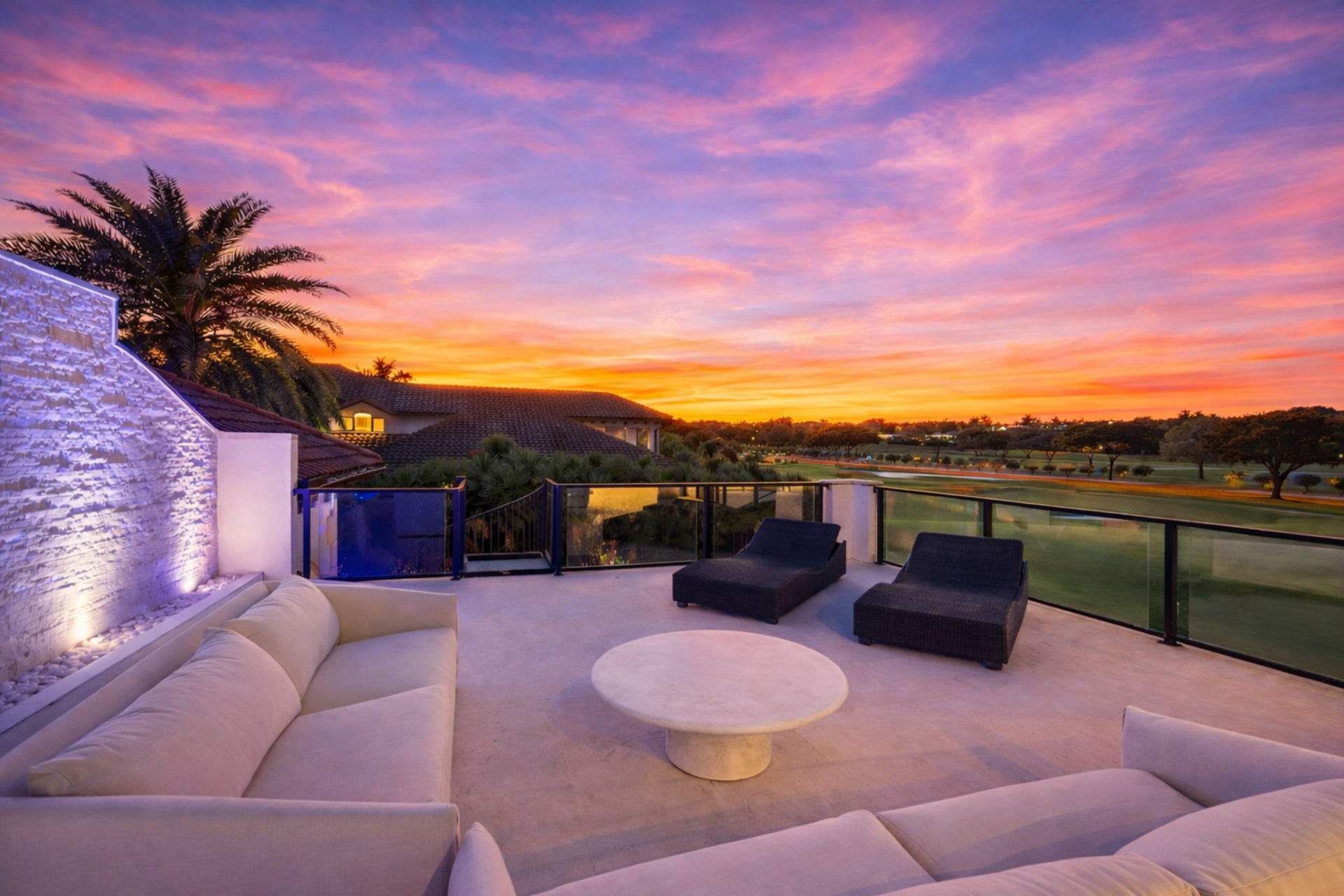 Right past the glass doors, a spacious private patio extends the suite outdoors, furnished for lounging and framed by glass railings that keep the sightlines uninterrupted across the fairways.