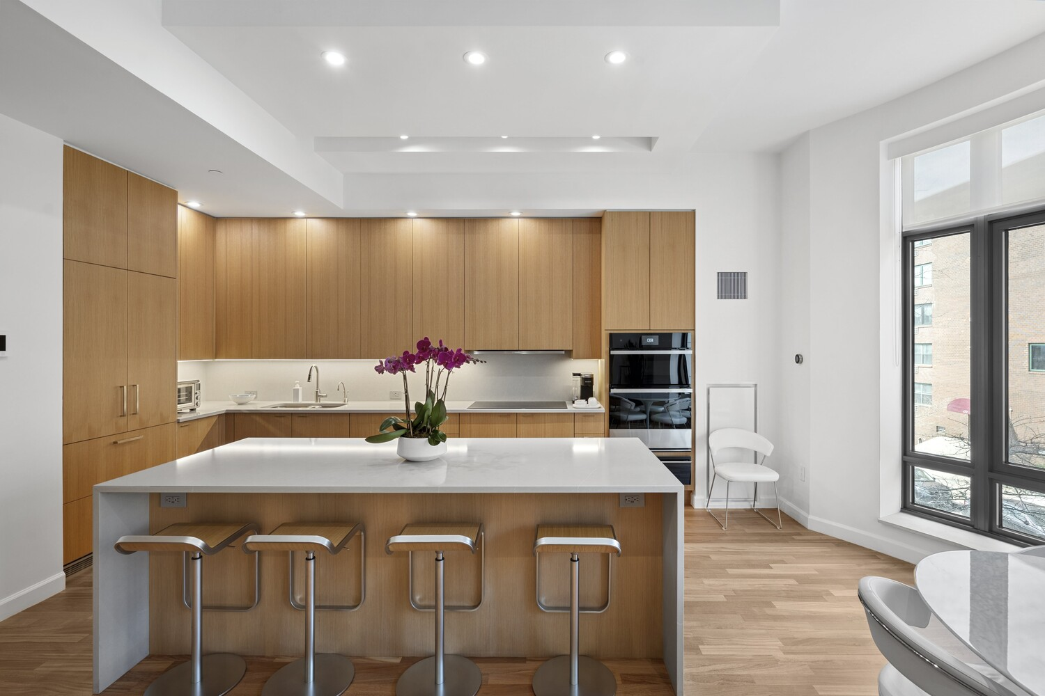 A streamlined kitchen with flat-front wood cabinetry and a long island sits closest to the windows.