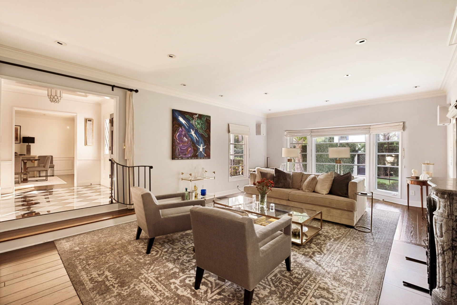 To the left of the black-and-white marble foyer, the formal living room opens on a slightly lower level, defined by rich hardwood floors and a wide picture window that frames the front yard. 
