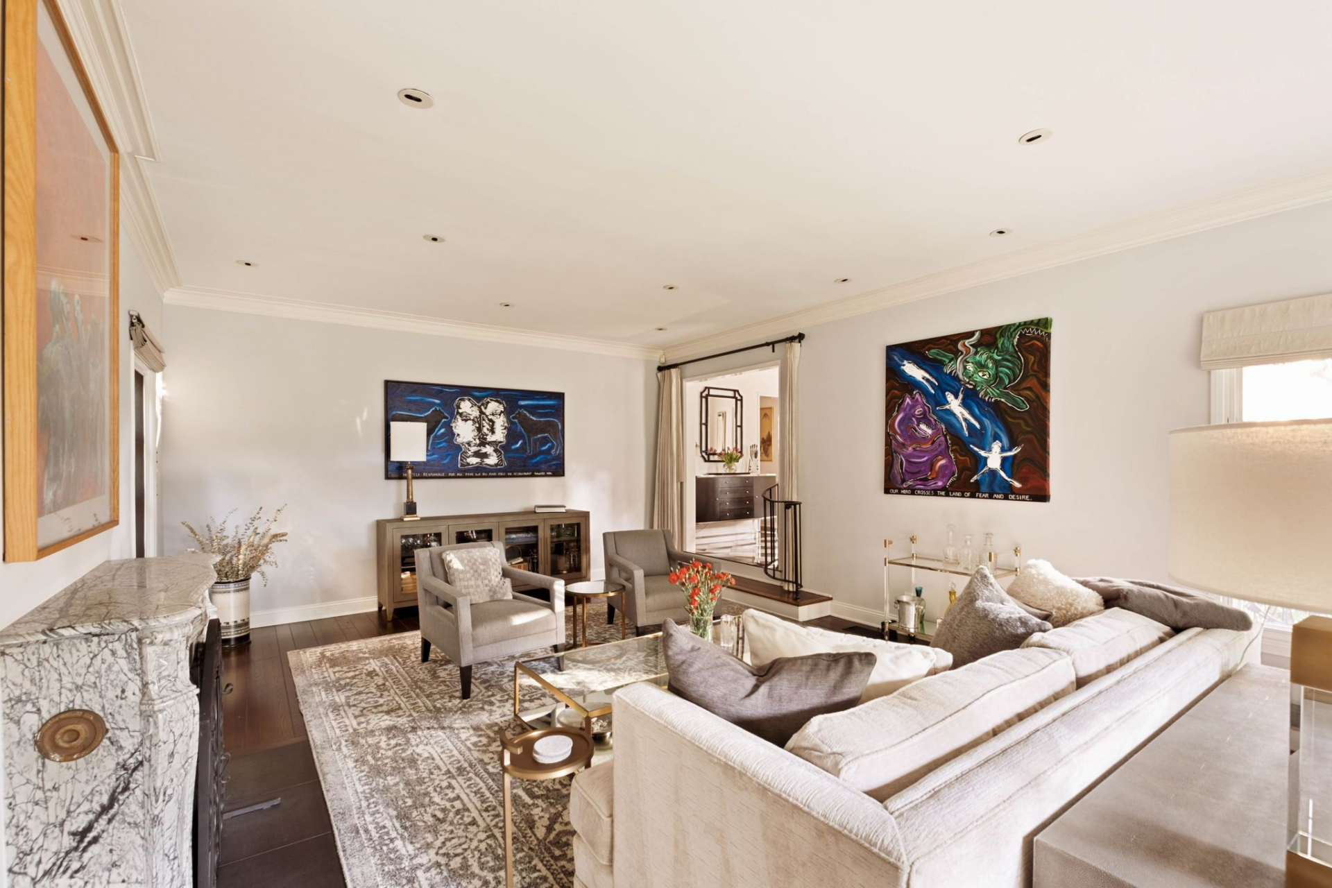 A neutral seating arrangement centers around a glass coffee table, with tailored armchairs and curated artwork adding color against the soft white walls.