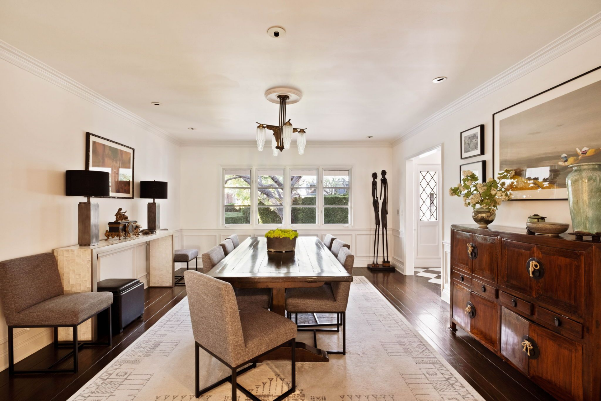A large wood dining table runs nearly the length of the room, surrounded by upholstered chairs and grounded by a patterned area rug that softens the clean lines. 