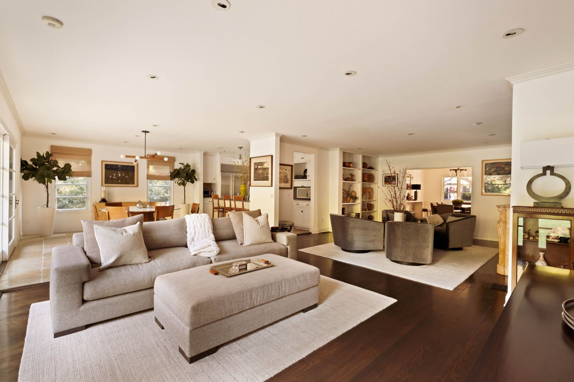 A grouping of curved lounge chairs forms a conversational circle atop a neutral rug, while wide-plank dark floors ground the space and French doors draw in views of the backyard. 