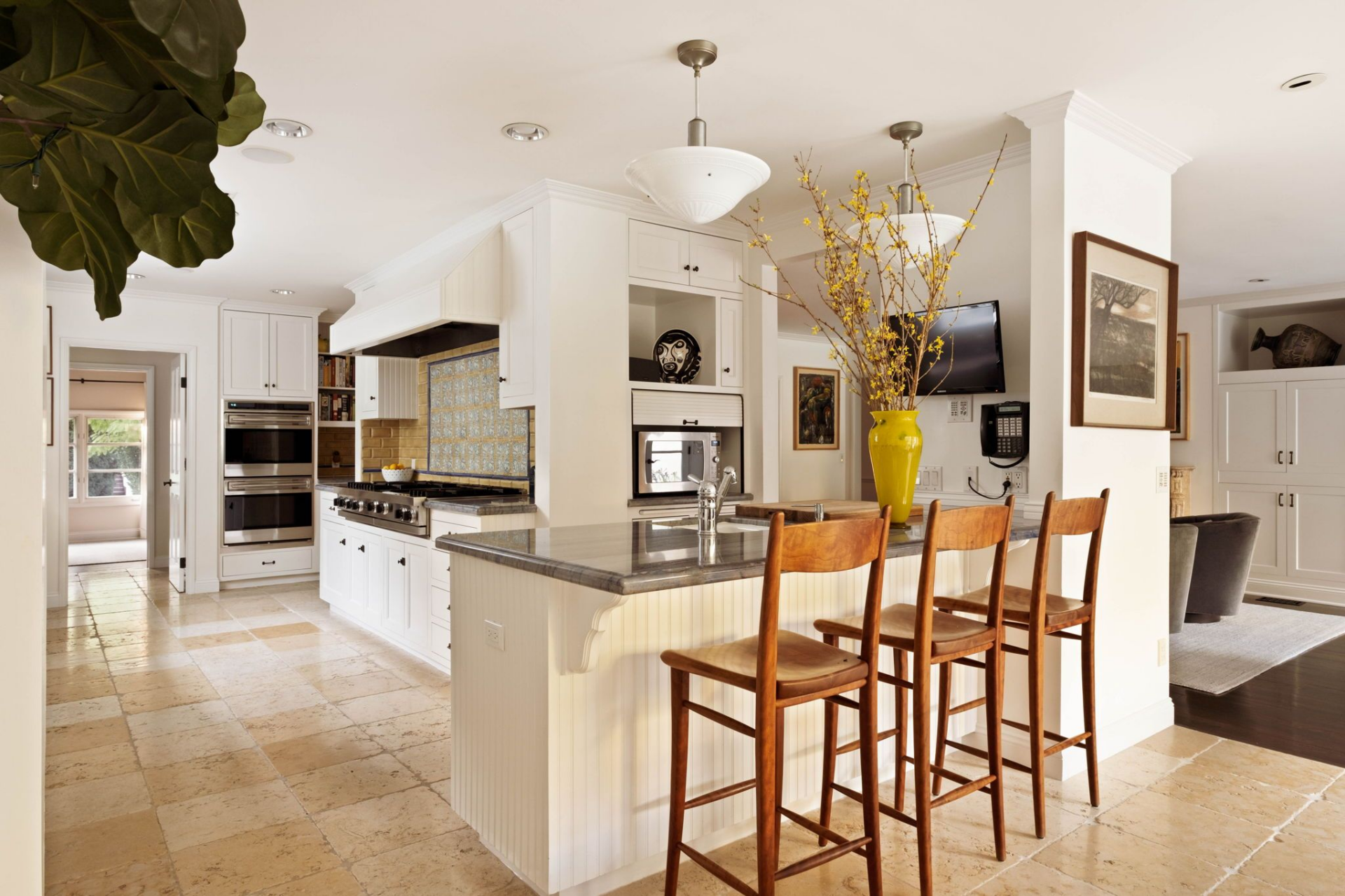 Behind the family room, the chef’s kitchen features creamy custom cabinetry, stone countertops, and a suite of professional-grade stainless appliances, including a double wall oven and a substantial gas range set beneath a detailed hood. 