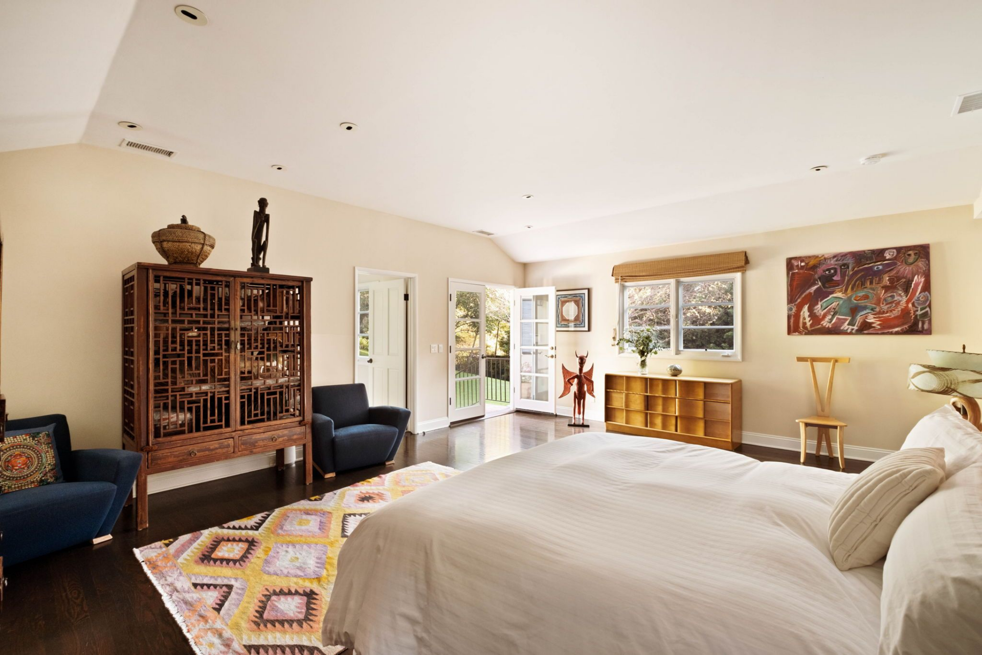 The primary suite occupies its own generous corner of the home, where dark hardwood floors run wall to wall and a wide bank of windows frames the greenery beyond. 