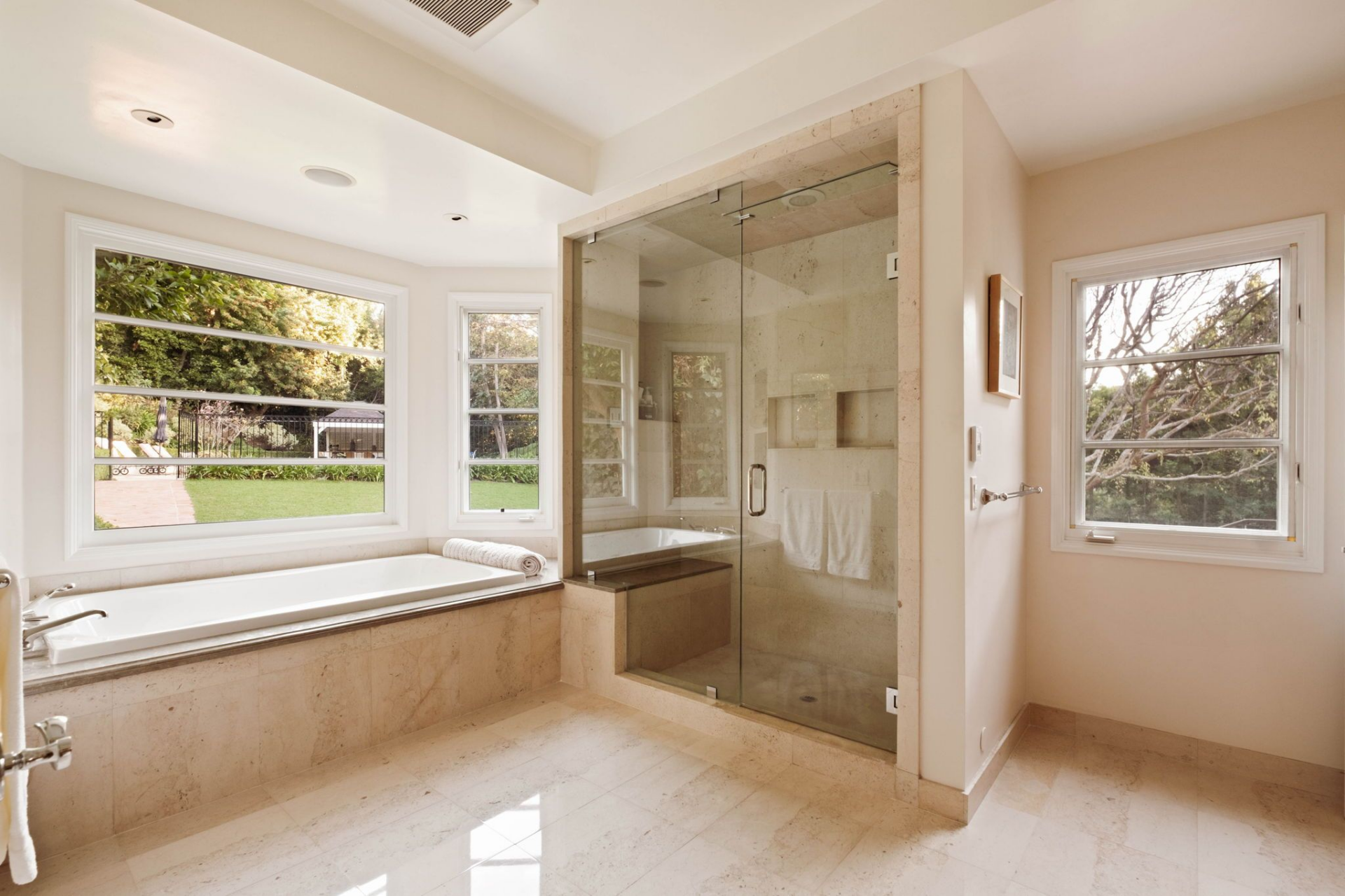 The suite's bathroom extends across warm stone heated floors with a deep soaking tub positioned beneath a trio of windows overlooking the yard and a glass-enclosed shower detailed with built-in niches.