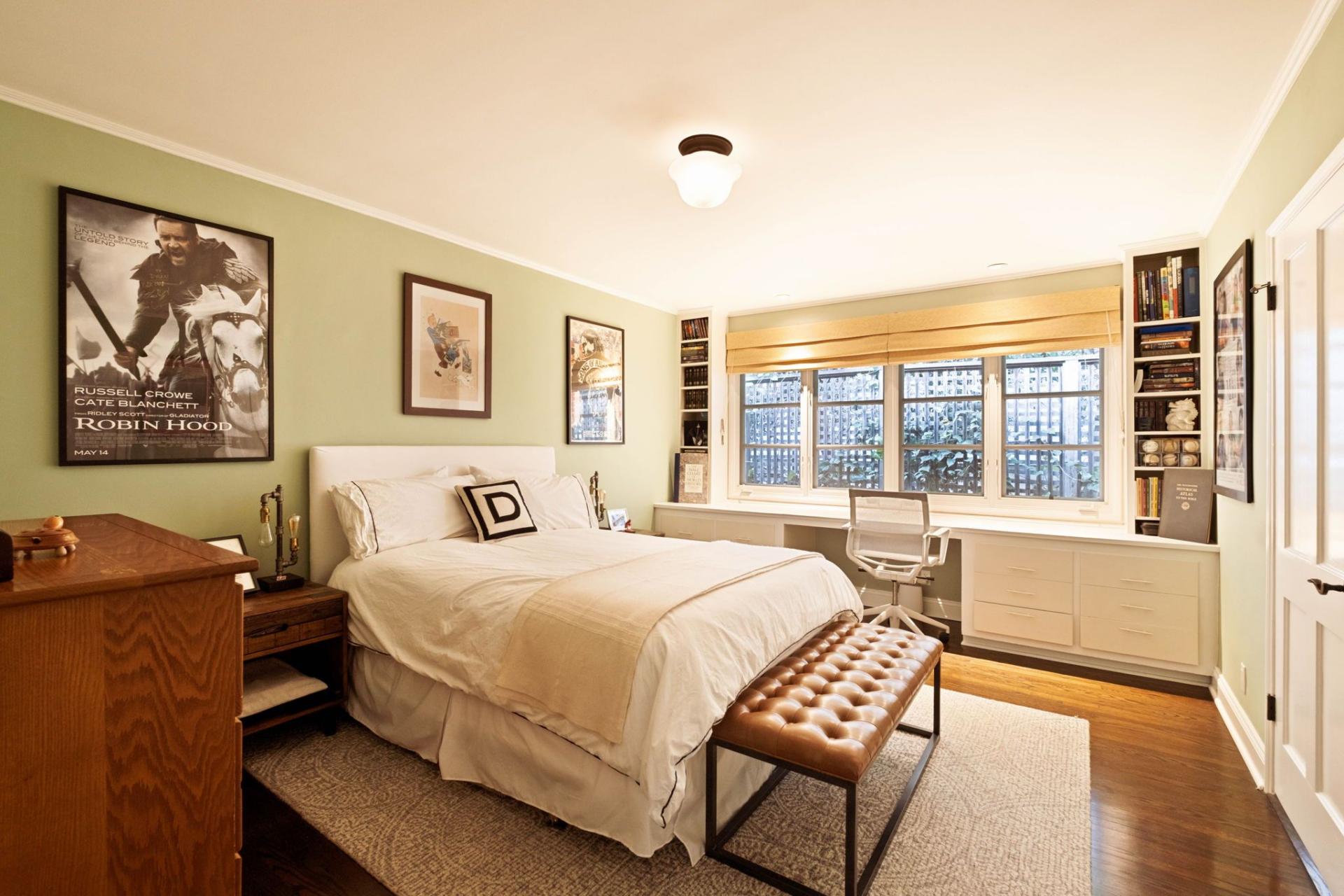 The bedroom features soft green walls, dark hardwood floors, and a built-in desk stretching beneath a wide bank of windows.