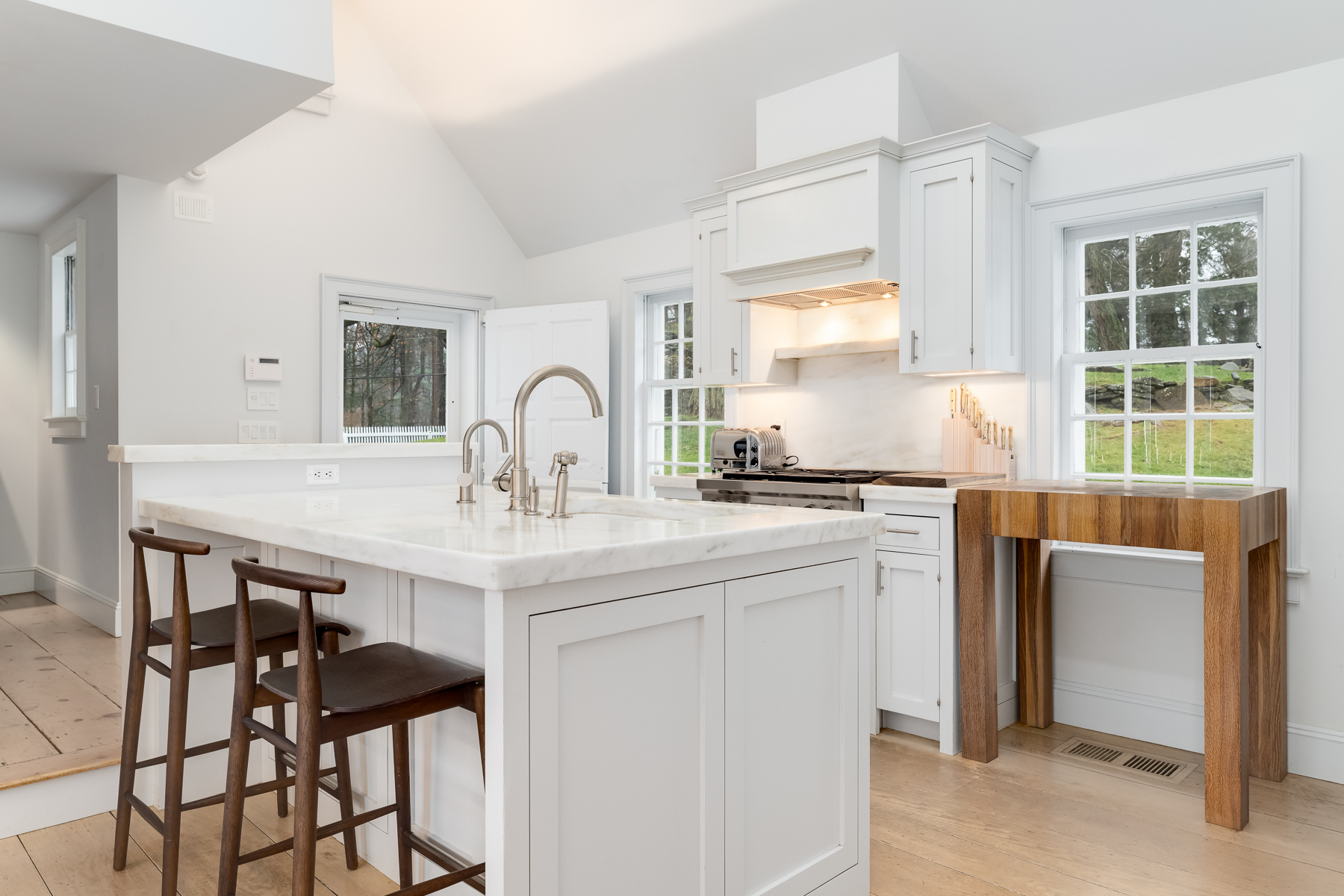 A large marble-topped island sits in the center, fitted with dual sinks and polished nickel fixtures, while two dark wood stools tuck neatly beneath the overhang for casual seating.
