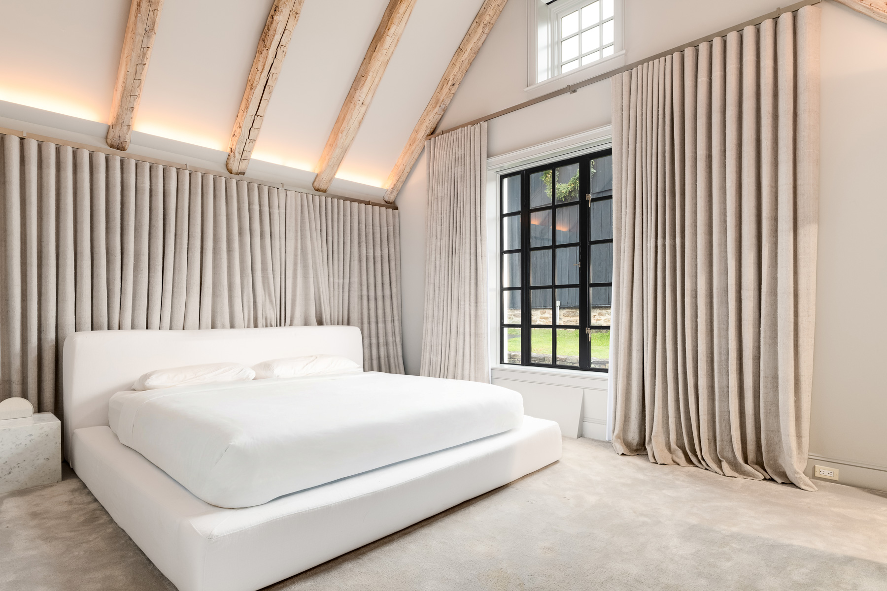The sleeping area itself is intentionally minimal, centered around a low-profile upholstered platform bed that enhances the height of the vaulted ceiling.