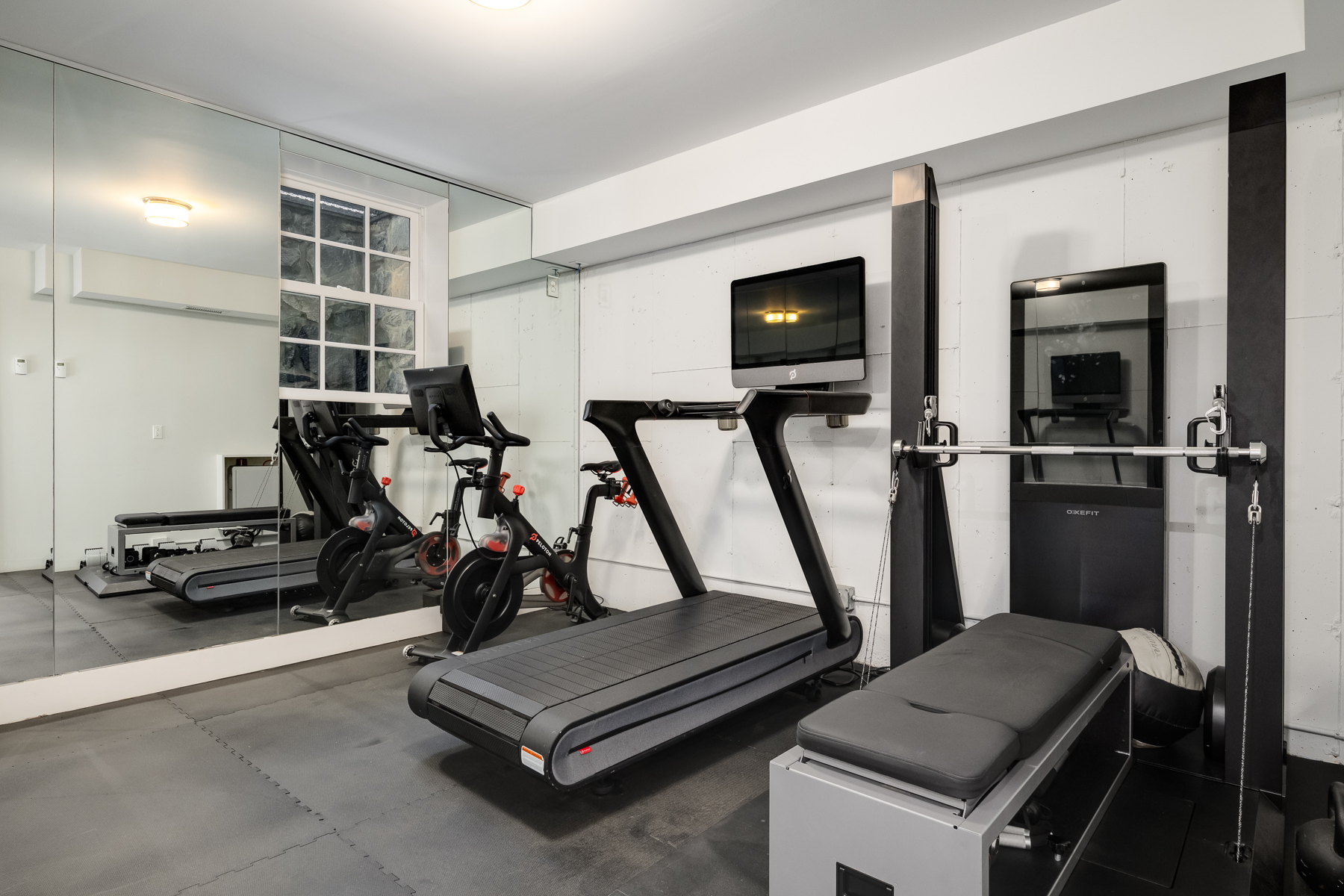 In the home gym, mirrored walls amplify the space, reflecting treadmills, stationary bikes, and spaces for weight lifting on top of the rubber flooring.