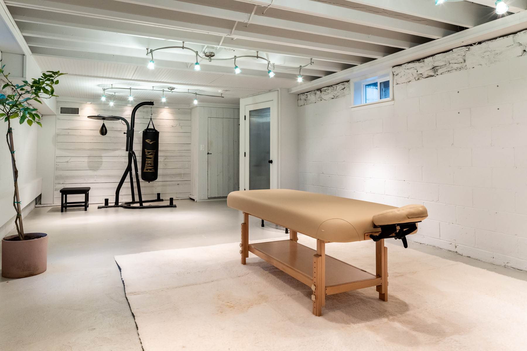 The boxing and recovery room adds another layer to the home’s wellness focus. A heavy bag anchors one end of the space, while the open floor area has a massage table in the center. 