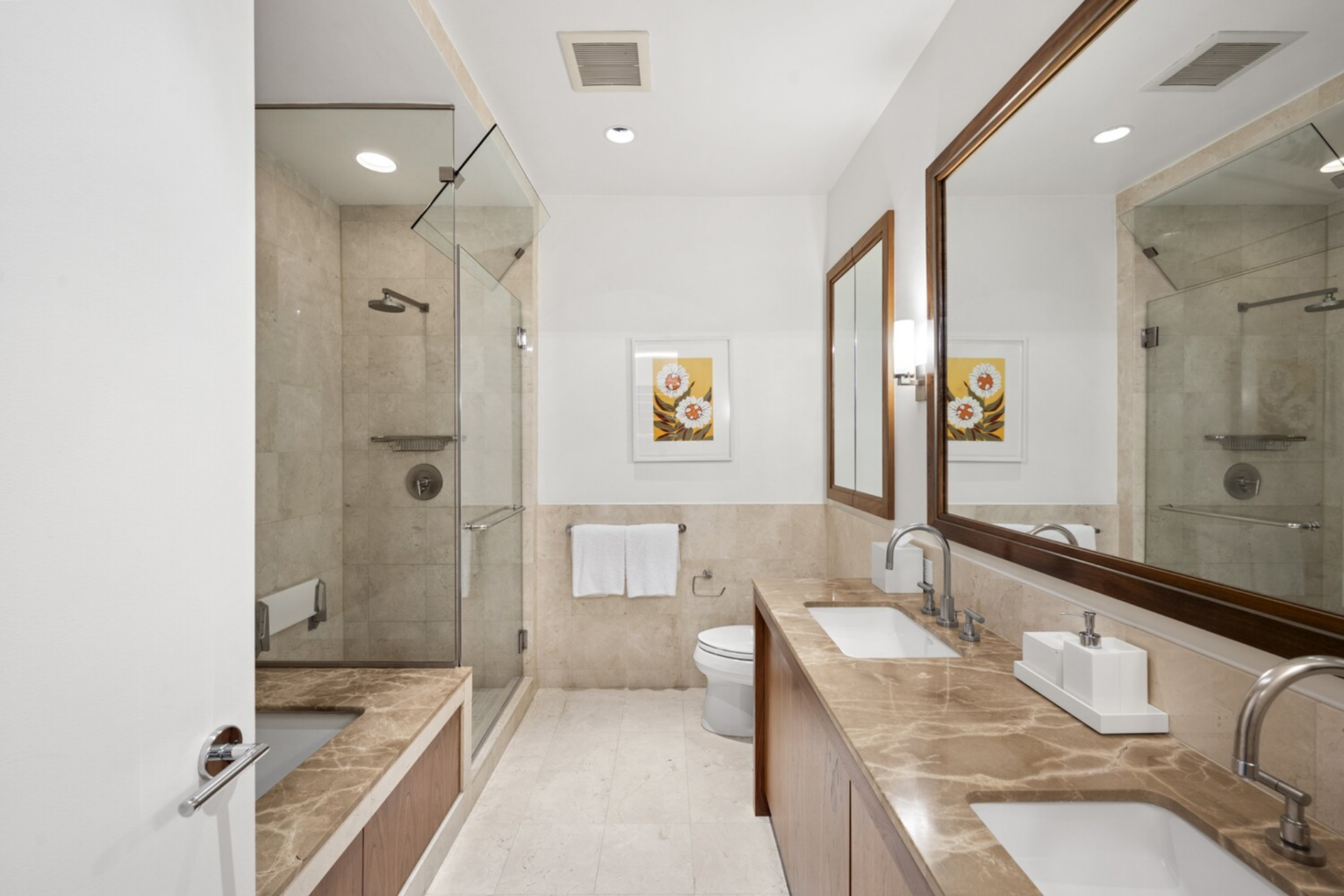 The en-suite bath is laid out with a full five-fixture configuration, including a glass-enclosed shower, a deep soaking tub, dual vanities with stone countertops, and carefully integrated lighting.