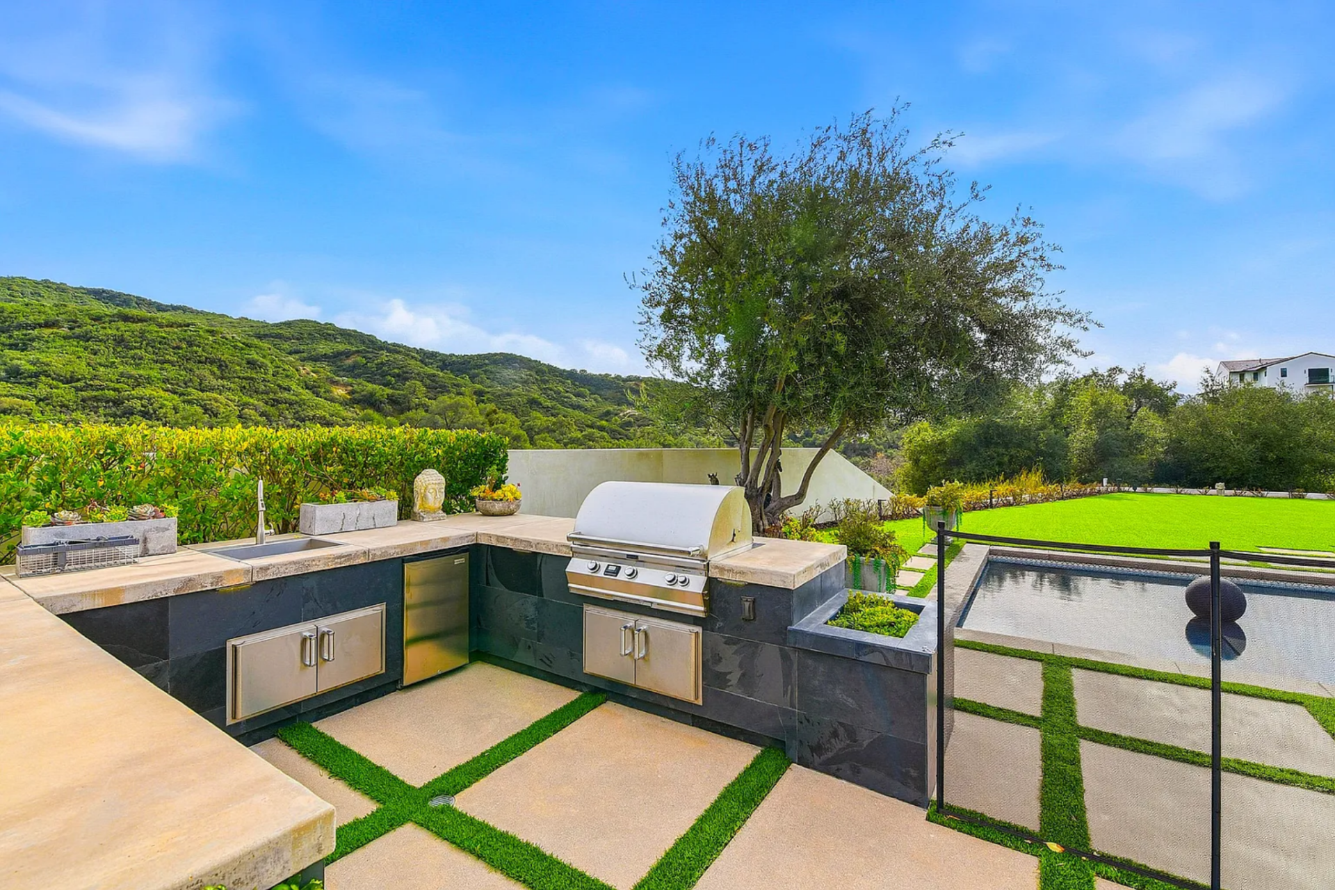 The station includes a professional-grade grill, under-counter refrigeration, sink, and prep space, all positioned to overlook the pool and lawn.