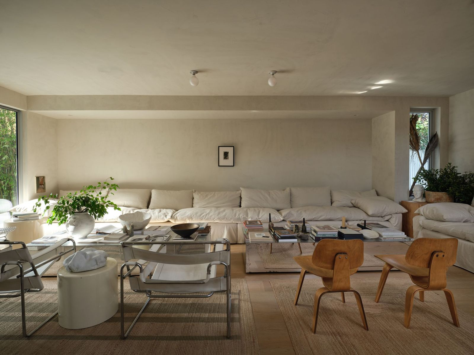 Iconic mid-century chairs introduce contrast with their sculptural wood frames and chrome detailing, balancing the softness of the upholstery with clean architectural lines. 