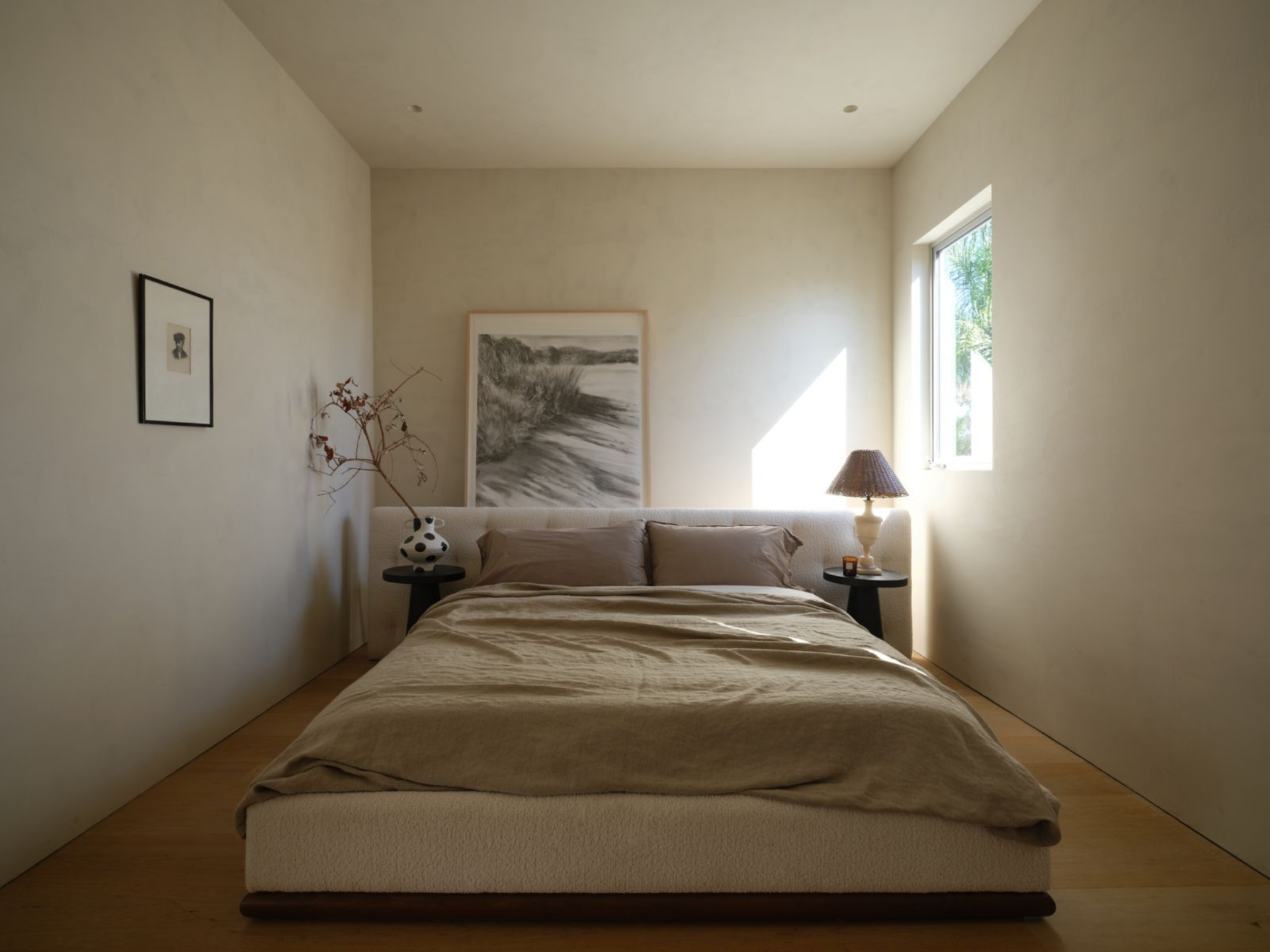 On an upper level, the primary suite begins in the bedroom with a low-profile upholstered bed sits flush against a simple backdrop, framed by petite black side tables that feel almost sculptural in their restraint. 