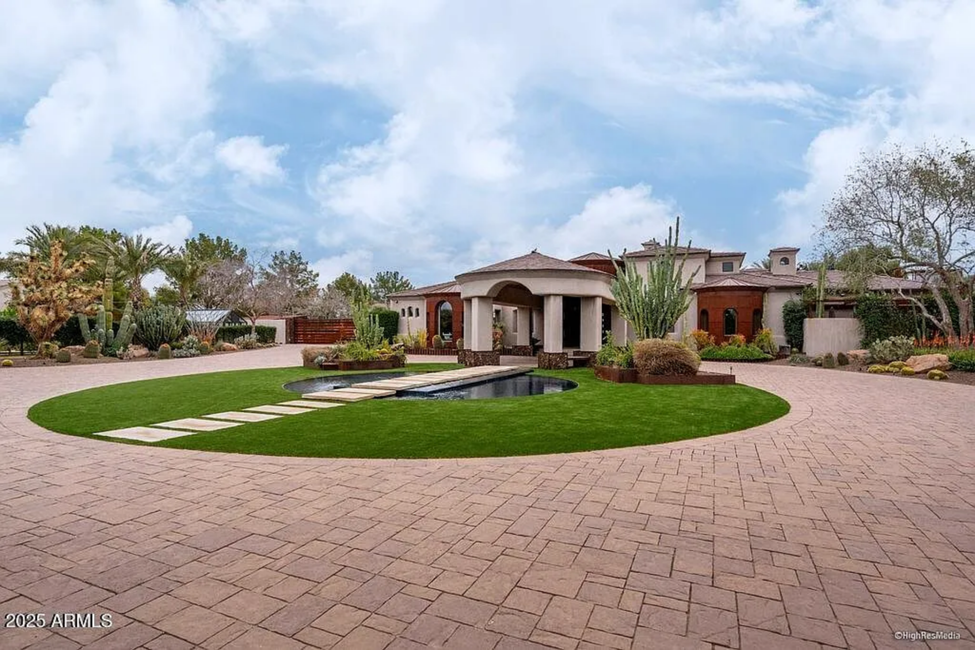 Before reaching the main house's front door, a sweeping paver motor court wraps around a circular lawn, where a sleek reflecting water feature and stepping stones create a dramatic focal point.