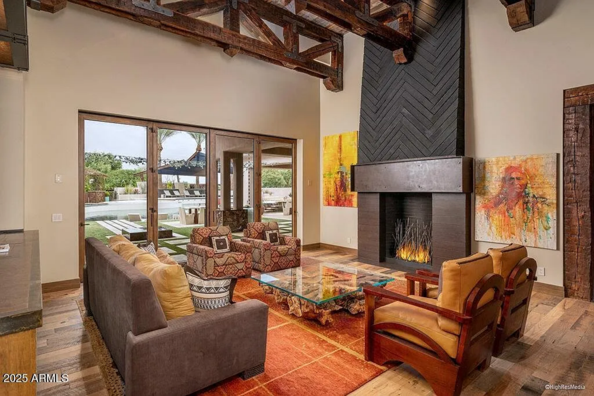Anchoring the space is a fireplace wrapped in dark herringbone detailing, framed by large-scale contemporary artwork that adds color just before the floor-to-ceiling glass doors.