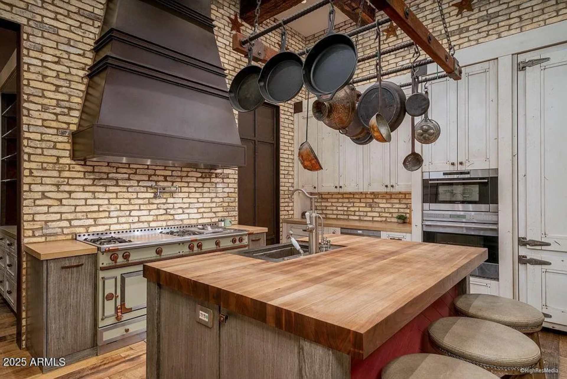The oversized range is framed by a dramatic metal hood and set against a full brick backsplash.