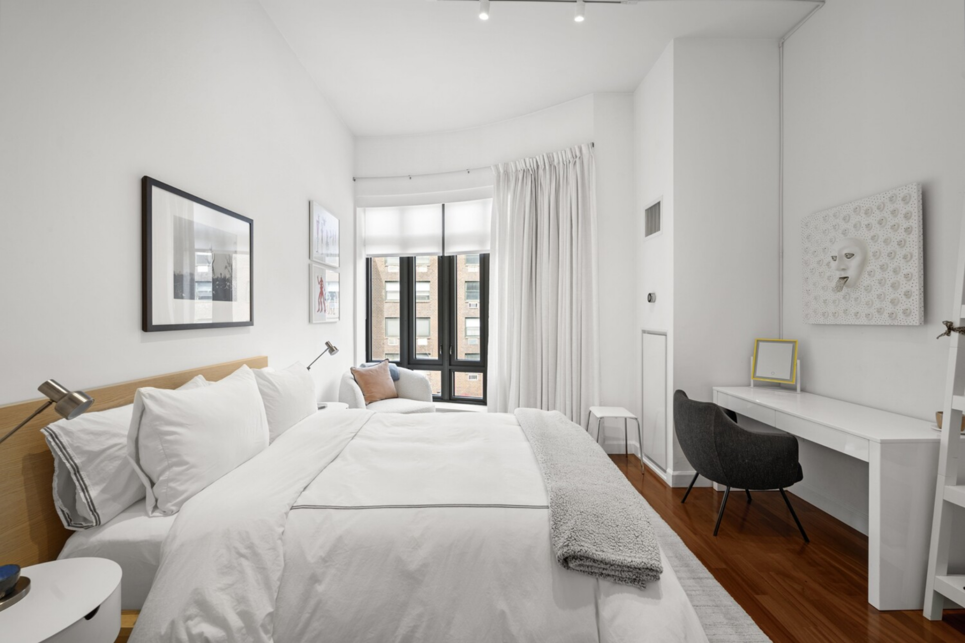 Positioned along the building’s curve, a simple platform bed is set atop warm wood floors, with space for a reading chair set near the window line.