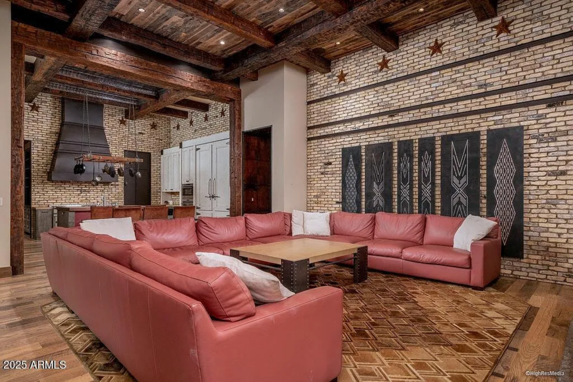 On the opposite side of the kitchen, the brick walls extend into the family room with a large red leather sectional wraps around a square wood-and-metal coffee table.